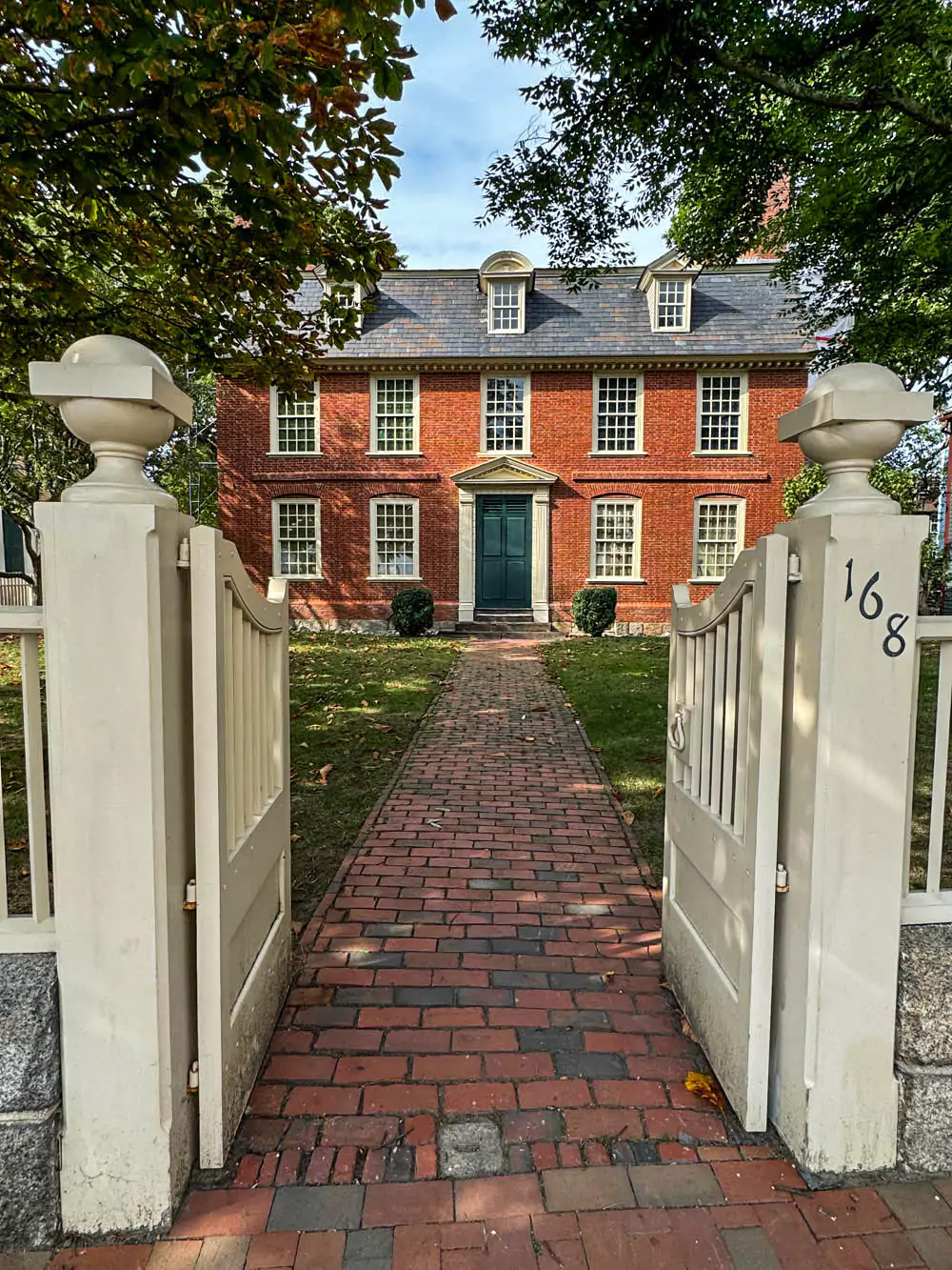 The grand Georgian-style Derby House in Salem, Massachusetts, featuring a symmetrical brick facade, white columns, and large multi-pane windows. The historic mansion stands as a well-preserved example of 18th-century architecture in the heart of Salem.