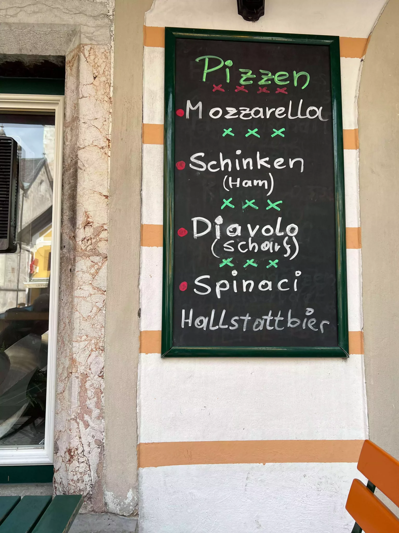 A restaurant menu displayed on a wall in Hallstatt, Austria, features neatly handwritten or printed items. The rustic background and traditional offerings reflect the cozy, alpine charm of the lakeside village.