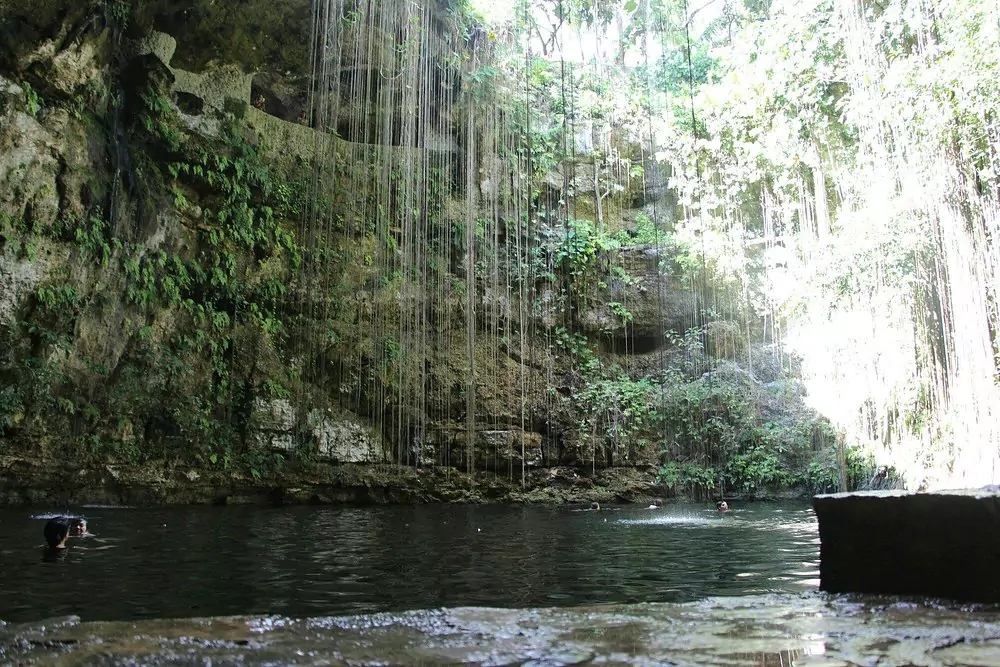 Cenote Ik Kil near Chichén Itzá in Mexico, featuring a deep natural sinkhole surrounded by hanging vines, rocky limestone walls, and clear blue water popular for swimming.