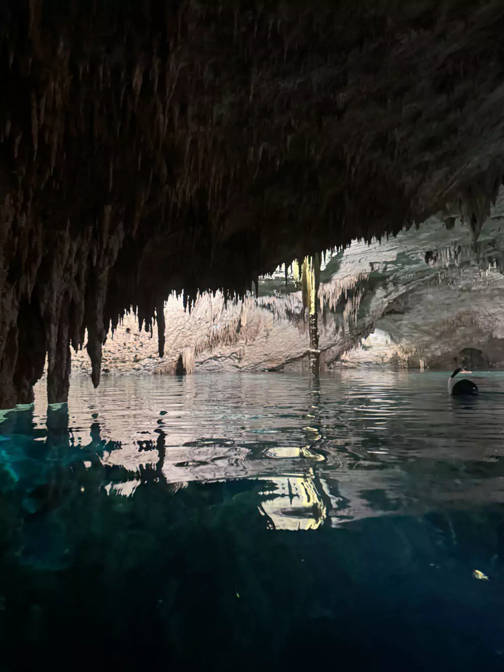 Cenote Taak Bi Ha in Mexico, an underground cenote featuring crystal-clear water, dramatic limestone formations, stalactites, and soft, filtered light creating a serene, otherworldly atmosphere.
