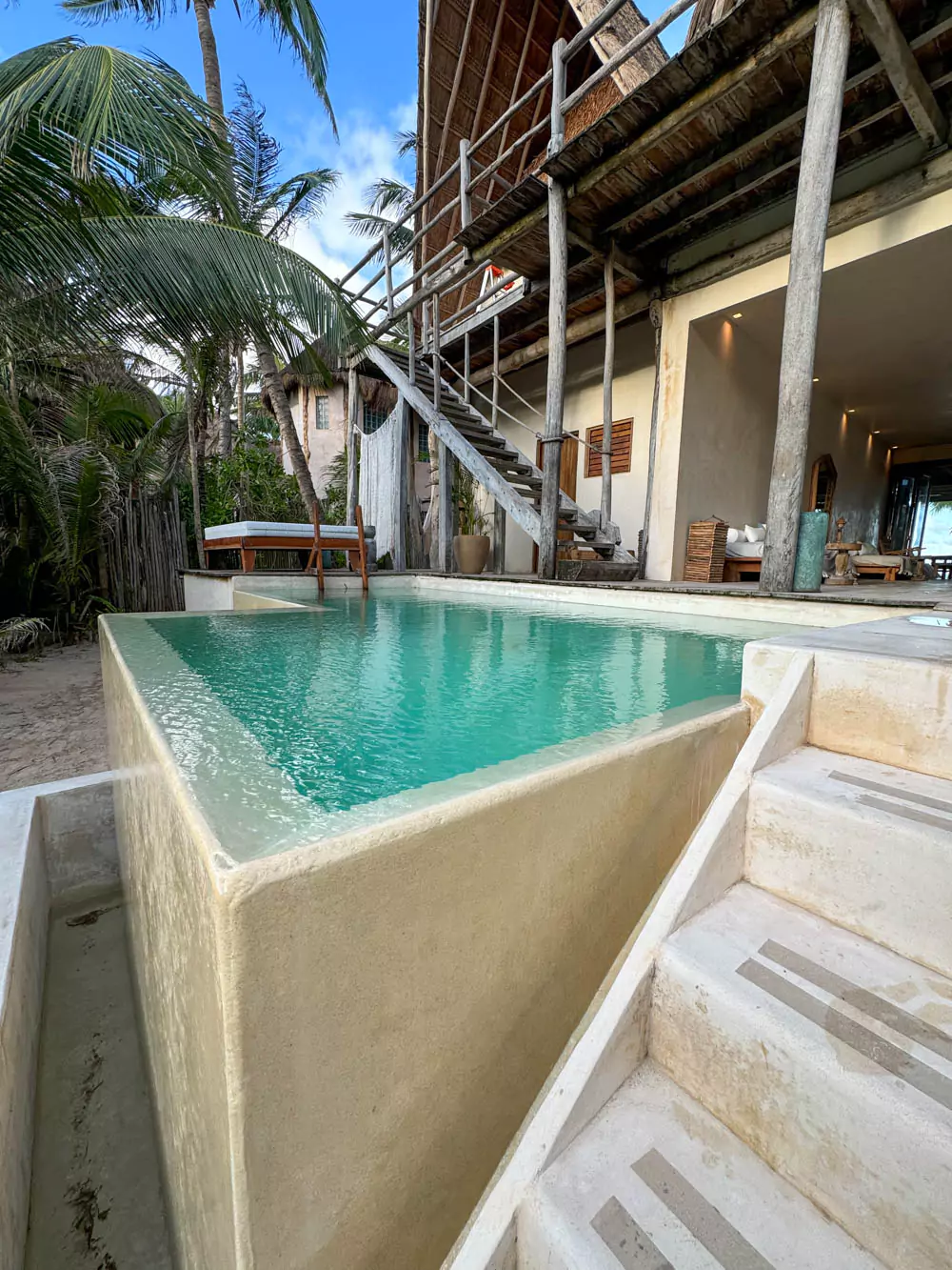 A tranquil infinity pool at La Valise Tulum hotel with crystal-clear water blending seamlessly into the horizon. The pool area is surrounded by tropical plants and offers peaceful views of the lush natural surroundings.