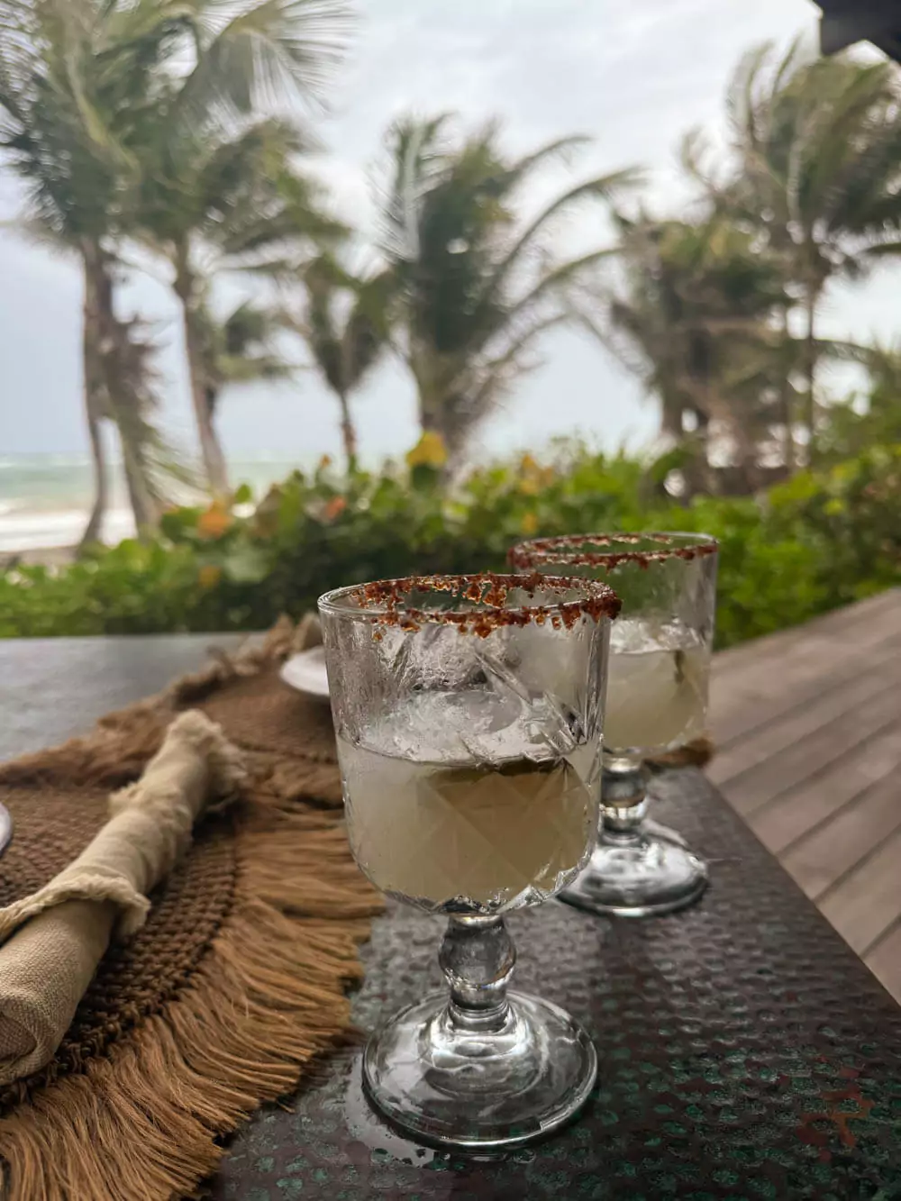 Refreshing margaritas served at La Valise Tulum, presented in salt-rimmed glasses with lime garnish, set on a rustic table with tropical scenery in the background.