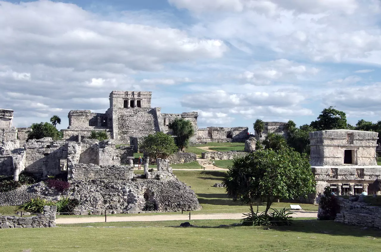 Ancient ruins of Tulum in Mexico, featuring stone structures perched on a cliff overlooking the Caribbean Sea, with remnants of the walled Mayan city framed by tropical vegetation and ocean views.