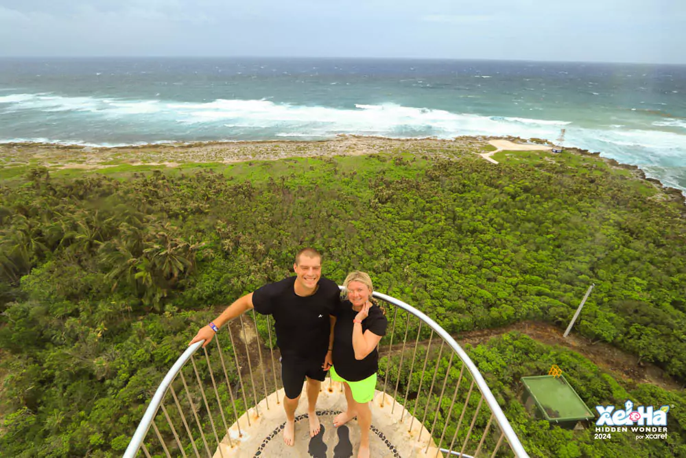 Clear blue lagoon at Xel-Há, a natural aquatic park in Mexico, teeming with colorful tropical fish swimming through crystal-clear water surrounded by lush greenery. Katie and Zack stand at the top of the park’s lighthouse, taking in panoramic views of the vibrant landscape and turquoise coastline.