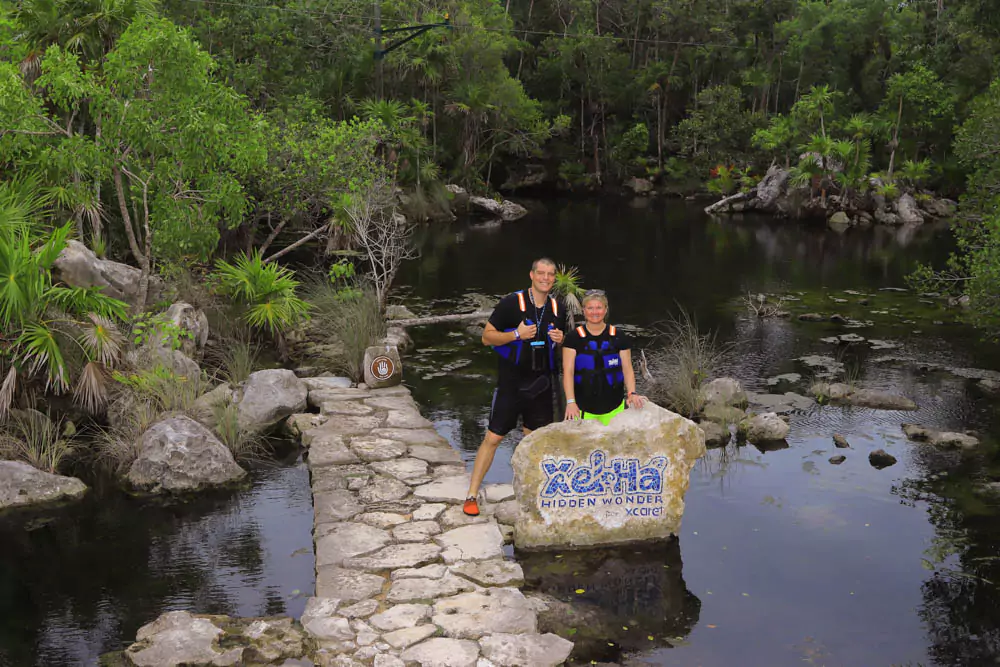 Katie and Zack at Xel-Há’s Hidden Wonder, smiling together beside crystal-clear water and lush greenery. The quiet, tucked-away spot offers a peaceful escape within the vibrant natural park setting.