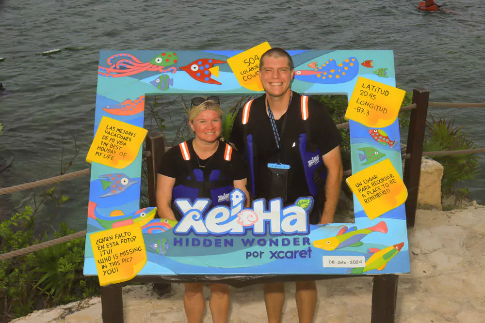 Katie and Zack at Xel-Há, standing together near a shaded, serene spot labeled “Hidden Wonder,” surrounded by lush tropical foliage and natural rock formations. The peaceful atmosphere highlights the beauty and tranquility of this secluded corner of the park.