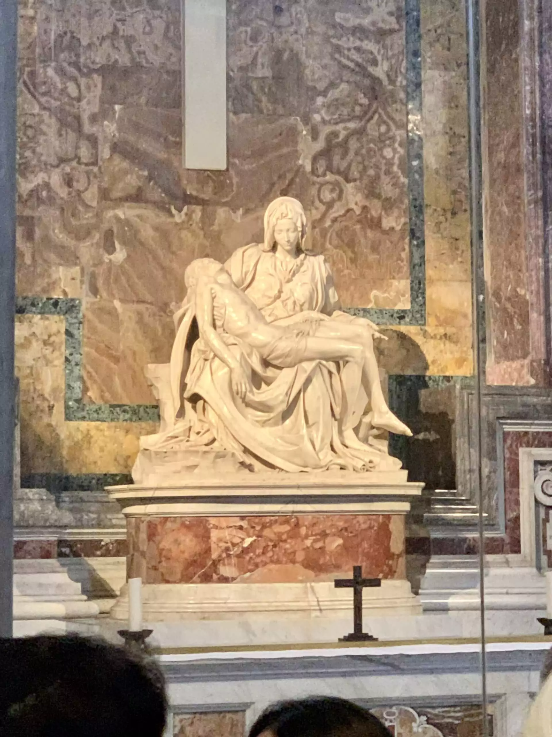 Michelangelo’s Pietà sculpture in St. Peter’s Basilica, Vatican City, depicting the Virgin Mary cradling the body of Jesus with intricate marble detail and emotional expression, displayed behind protective glass.