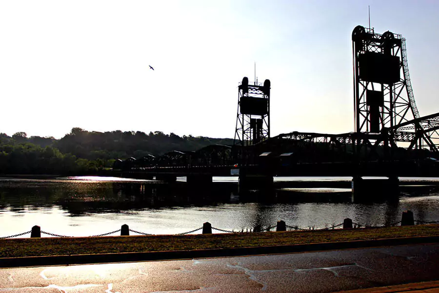 Stillwater Lift Bridge in Minnesota, featuring its steel truss design spanning the St. Croix River with scenic views of the water and surrounding greenery. The historic bridge, once used for vehicle traffic, now serves pedestrians and cyclists in a charming riverside setting.