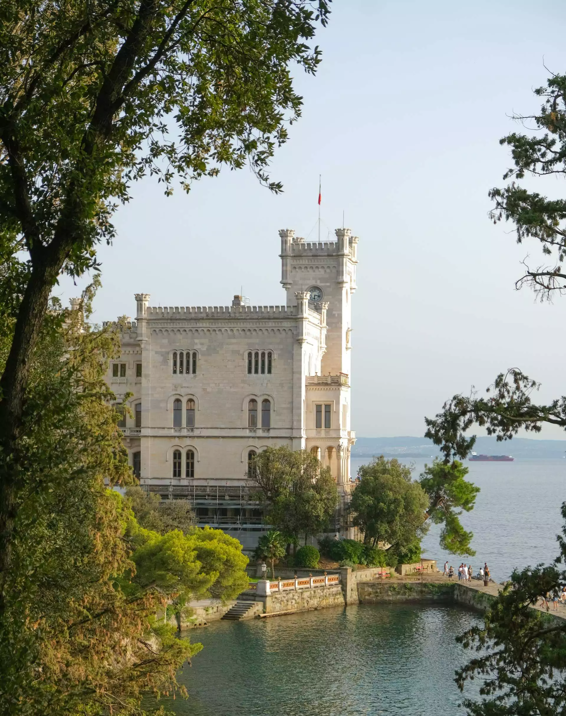 Miramare Castle on the Gulf of Trieste, Italy, perched on a rocky coastline with white limestone architecture, surrounded by lush gardens and overlooking the sparkling blue Adriatic Sea.