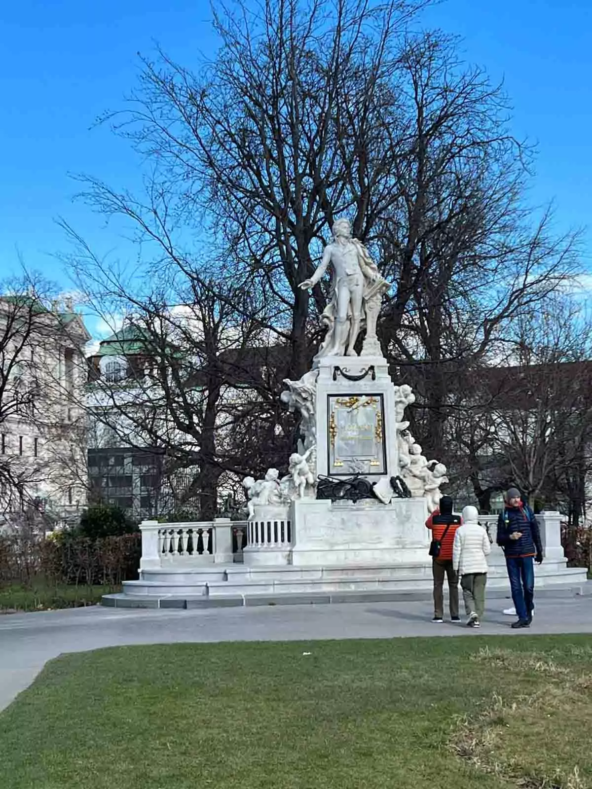 Statue of Wolfgang Amadeus Mozart in Vienna, Austria, set in Burggarten park, featuring the composer in a graceful pose atop a decorated pedestal with musical motifs and blooming flowers nearby.
