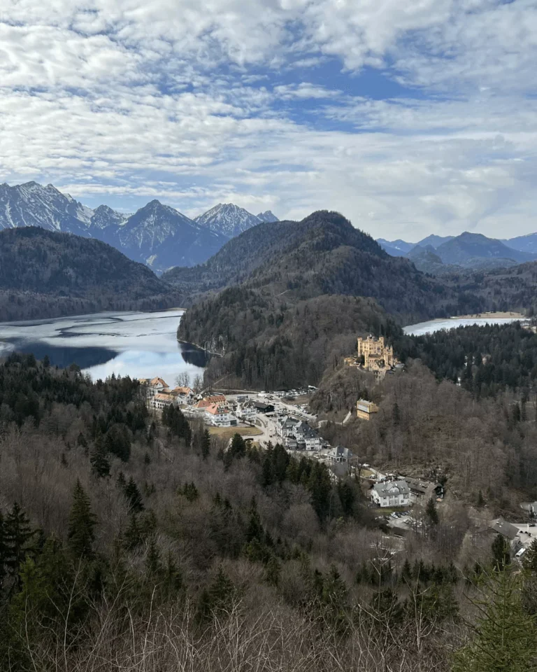 Panoramic view from Neuschwanstein Castle in Bavaria, Germany, overlooking Hohenschwangau Castle nestled in the trees and the expansive Schwangau Valley with its alpine lakes and rolling hills.