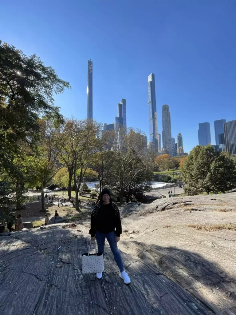 Top Attractions in New York City - Katie Kinsley lounging on a large rock in Central Park, surrounded by lush greenery and shaded by nearby trees. She appears relaxed and content, soaking in the peaceful atmosphere amid the natural escape of the city.
