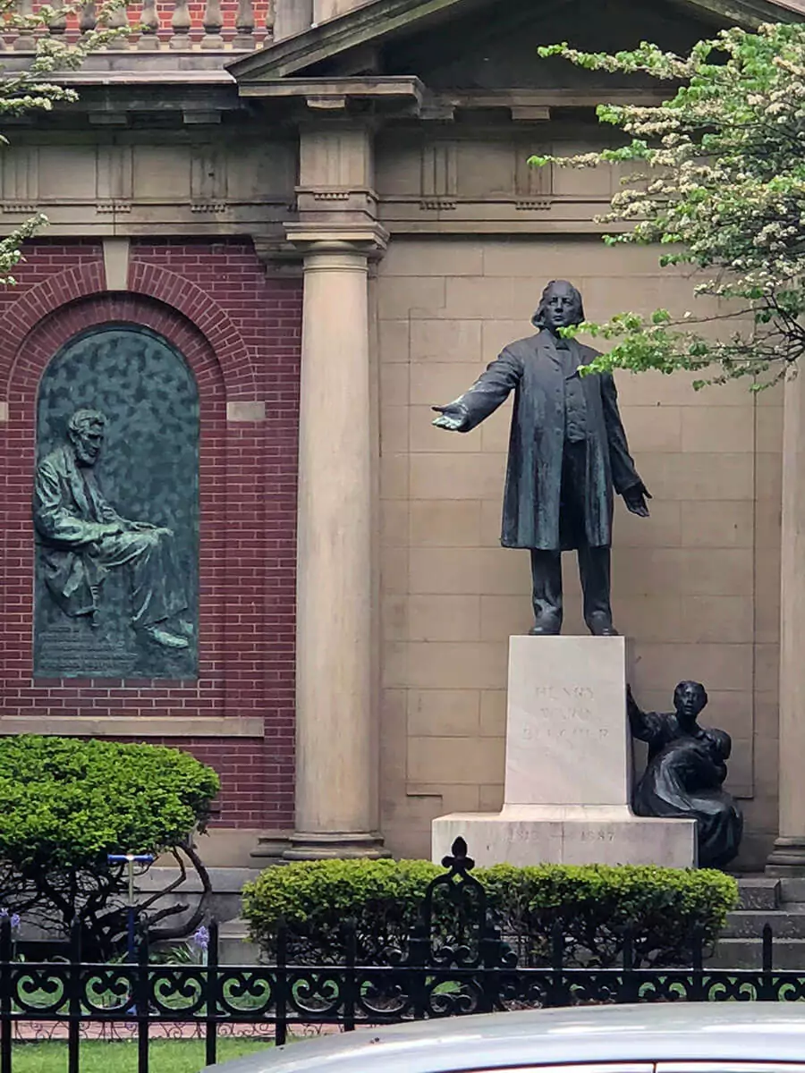 Statue outside Plymouth Church in Brooklyn, New York, depicting a historic figure in a contemplative pose. The sculpture stands near the church’s brick facade and leafy surroundings, honoring the site's deep ties to abolitionist history and community leadership.