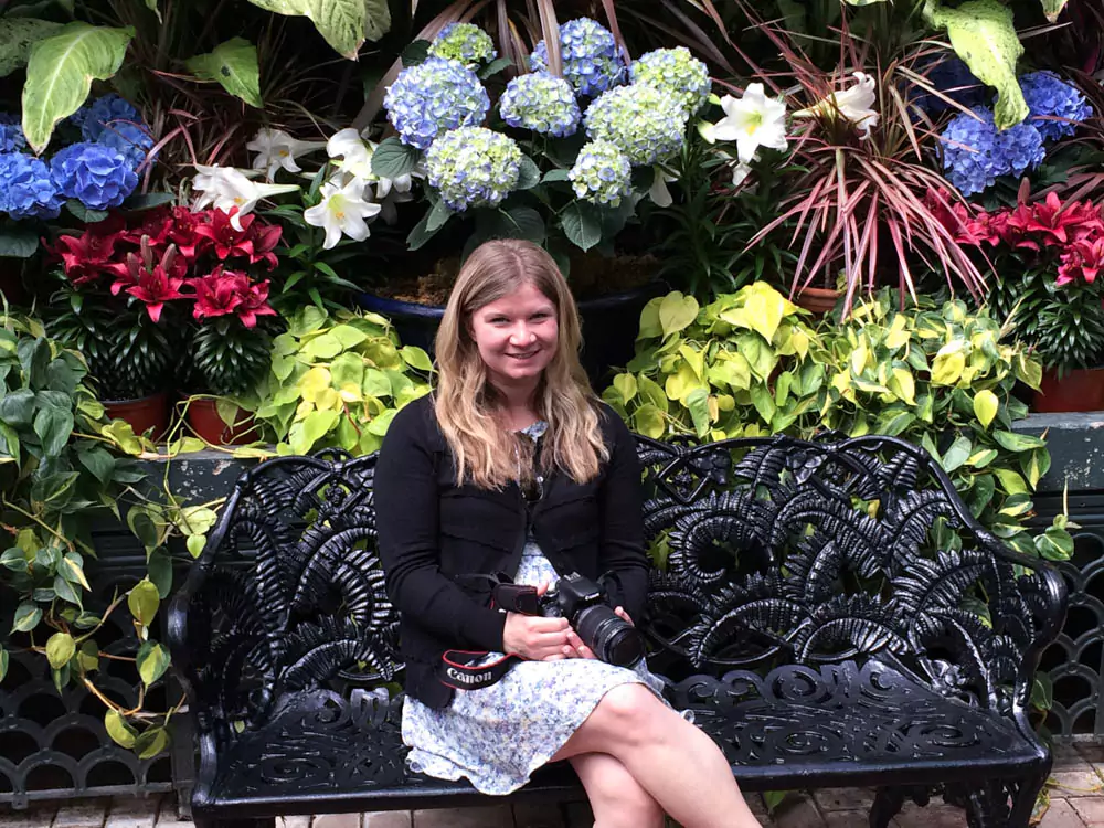 Katie smiling in a beautifully manicured garden at the Biltmore Estate in Asheville, North Carolina, surrounded by colorful flowers and lush greenery. The elegant landscaping highlights the estate’s historic charm.