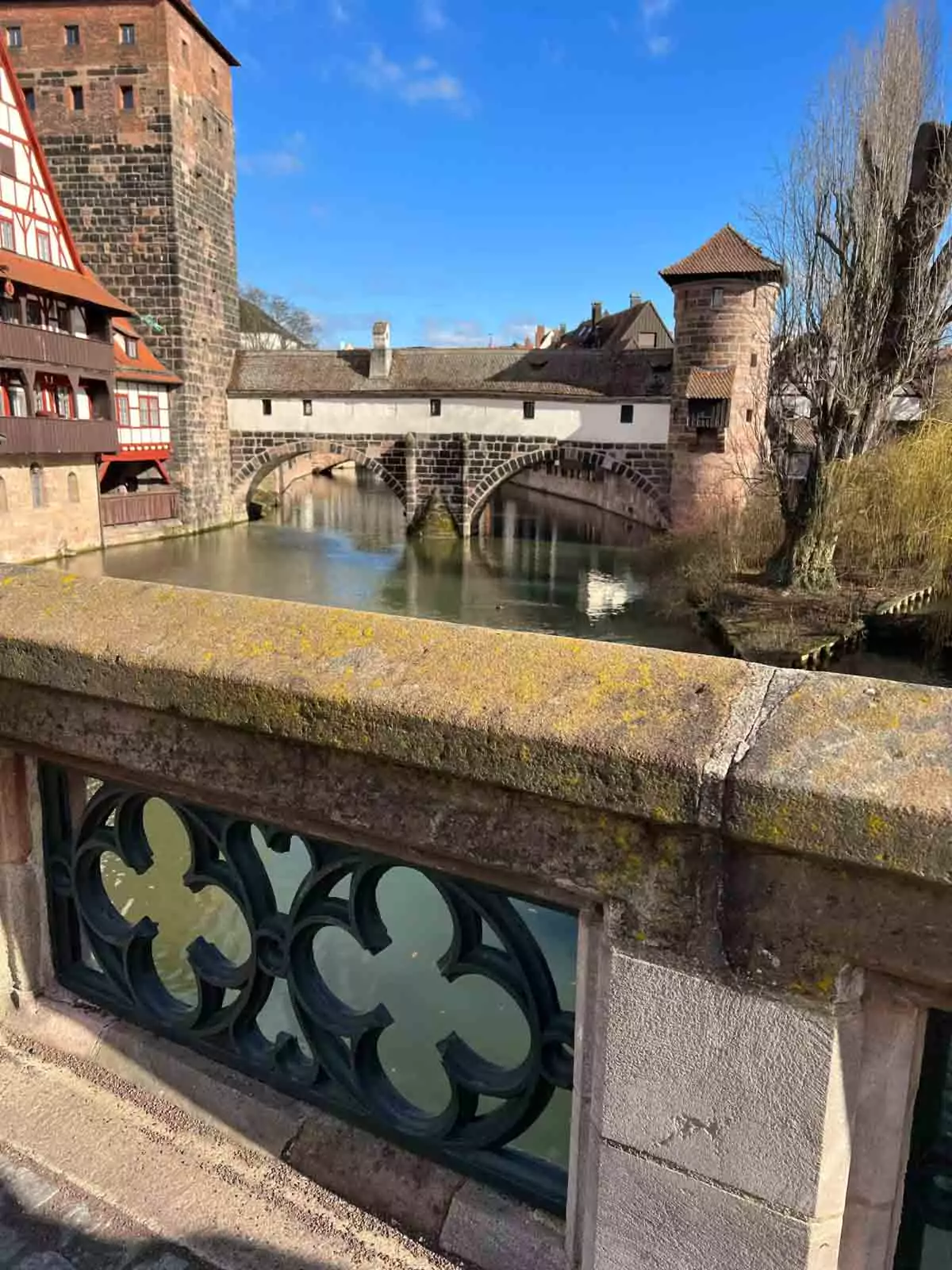Scenic view of the Pegnitz River from Maxbrücke Bridge in Nuremberg, Germany, with reflections of historic buildings, arched stone bridges, and timber-framed houses lining the waterfront.