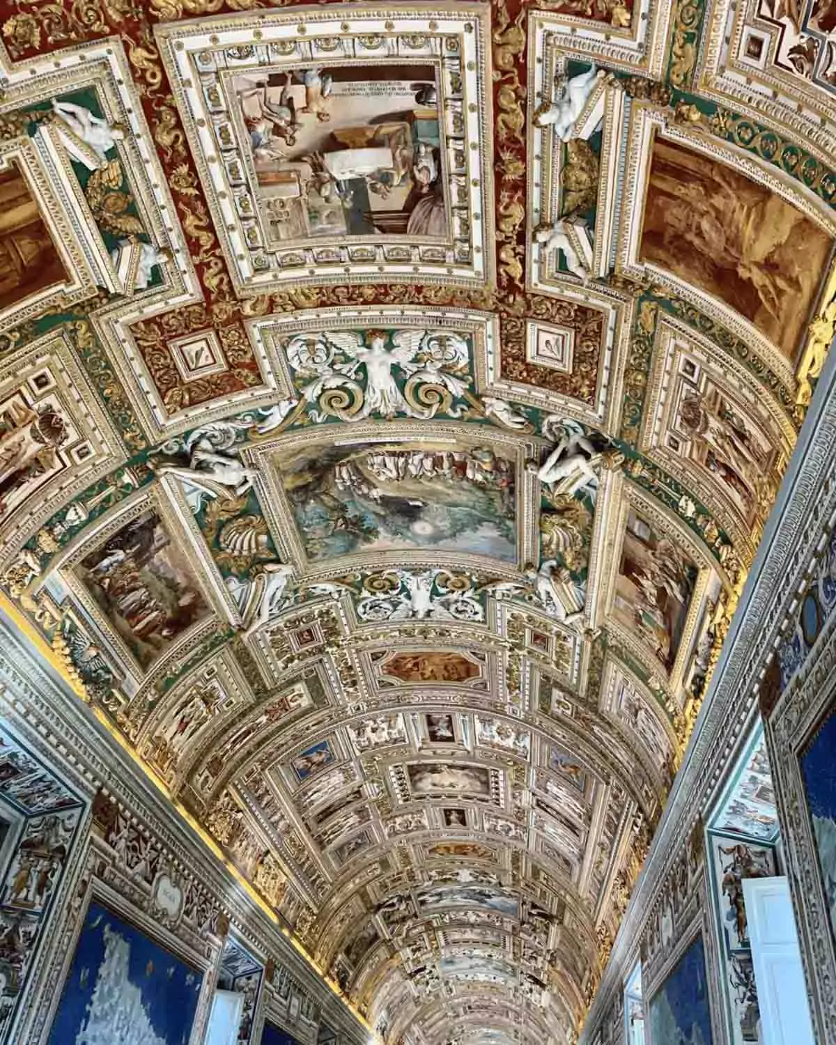 Ornate ceiling in the Vatican Museums’ Gallery of Maps, featuring intricate gold detailing, vibrant frescoes, and elaborate architectural designs that stretch the length of the hallway.