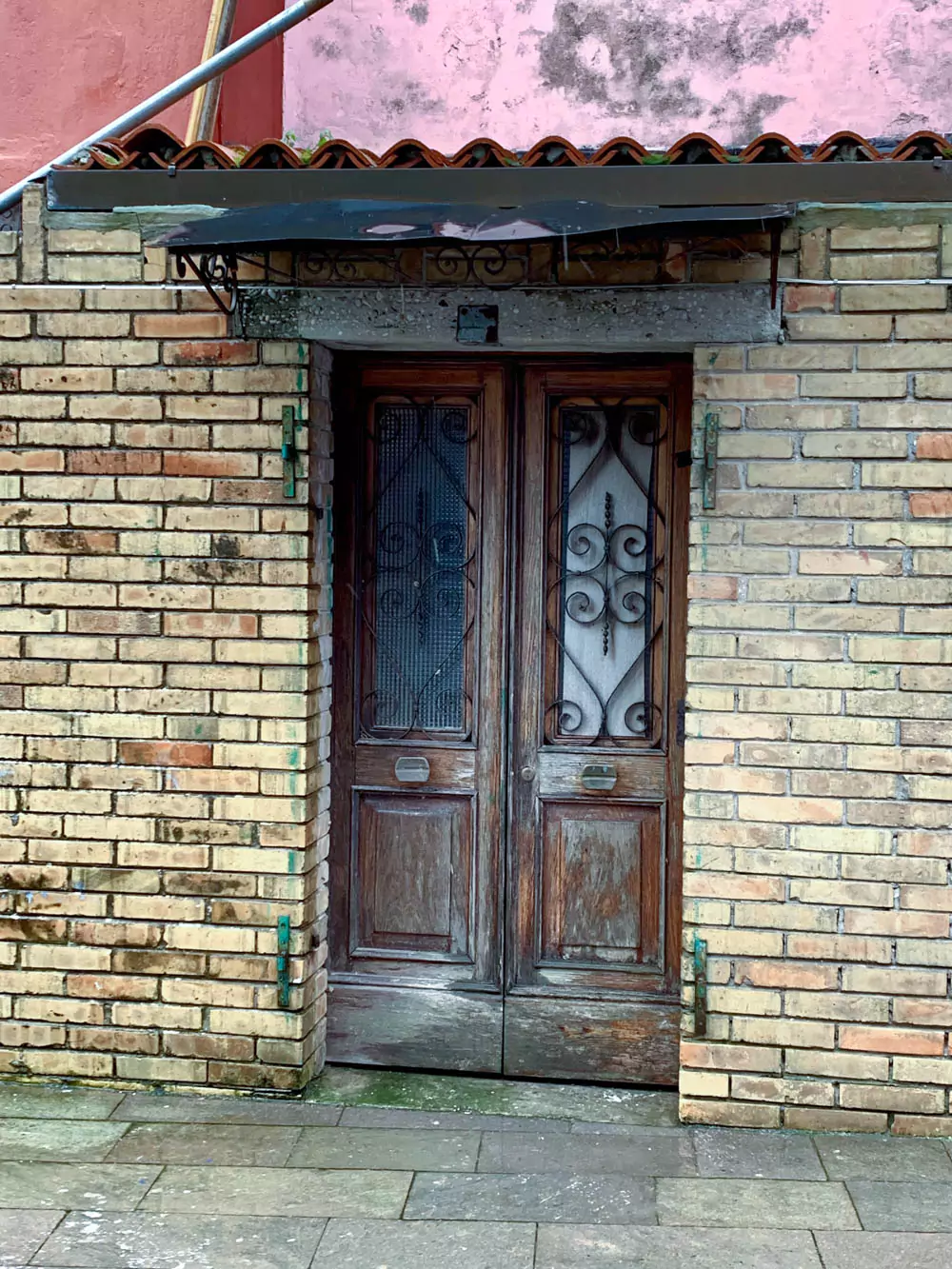 An ornate wooden door with intricate carvings stands set into a tan brick building in Burano, Italy. The rich wood contrasts with the soft, sun-washed bricks, blending elegance with the island’s rustic charm.