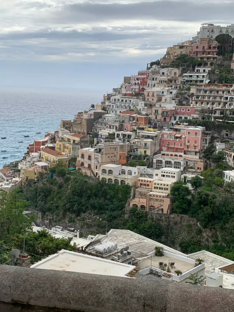 Scenic view of Positano, a picturesque village on Italy’s Amalfi Coast, with pastel-colored buildings stacked along steep cliffs, overlooking the Mediterranean Sea and lined with vibrant bougainvillea.