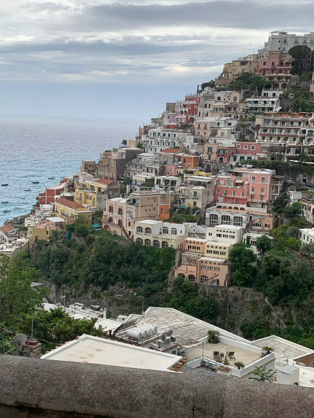 Scenic view of Positano, a picturesque village on Italy’s Amalfi Coast, with pastel-colored buildings stacked along steep cliffs, overlooking the Mediterranean Sea and lined with vibrant bougainvillea.