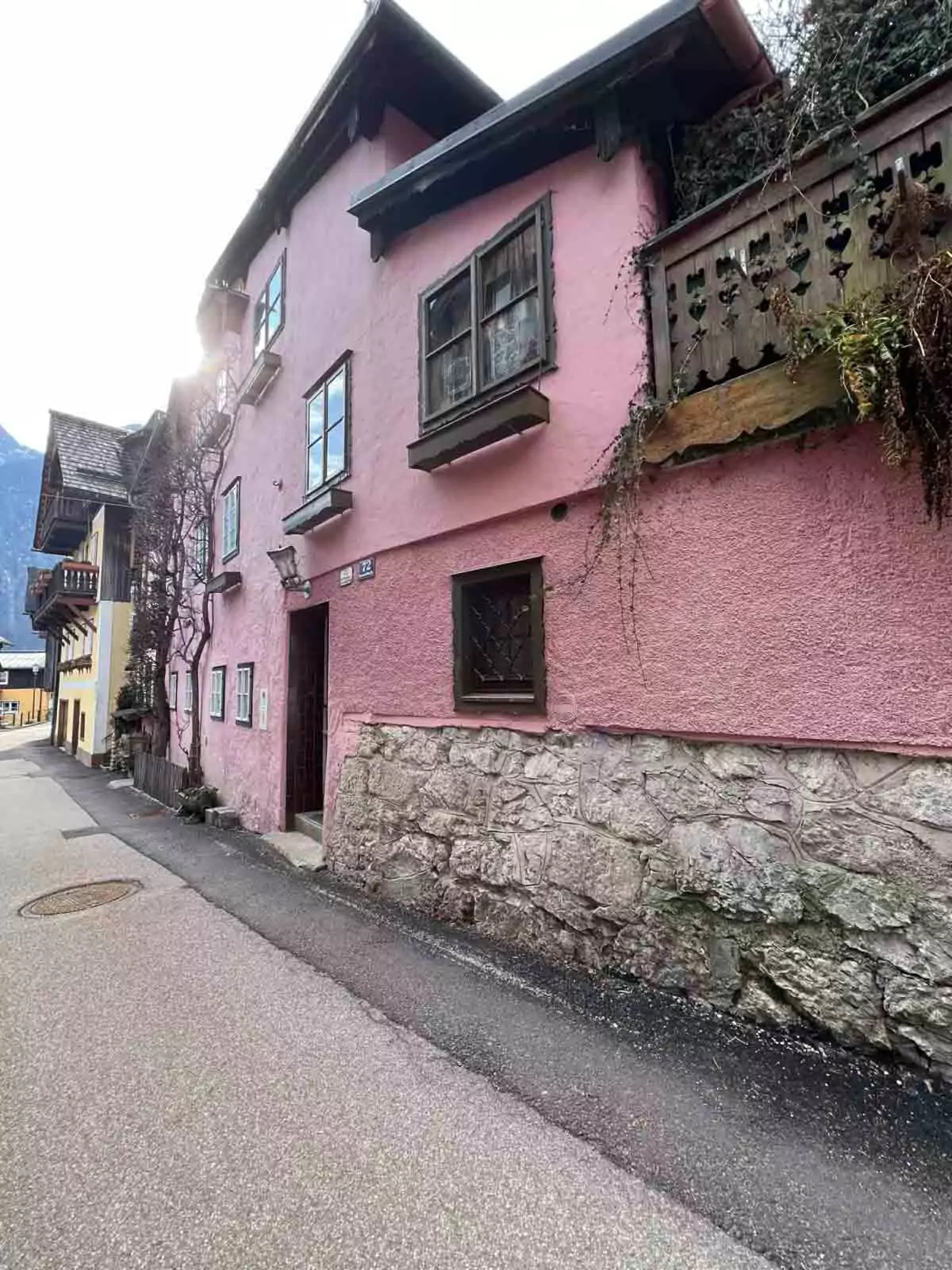 Charming pink building in Hallstatt, Austria, with white-trimmed windows, wooden balconies, and alpine details, nestled among the colorful village facades.
