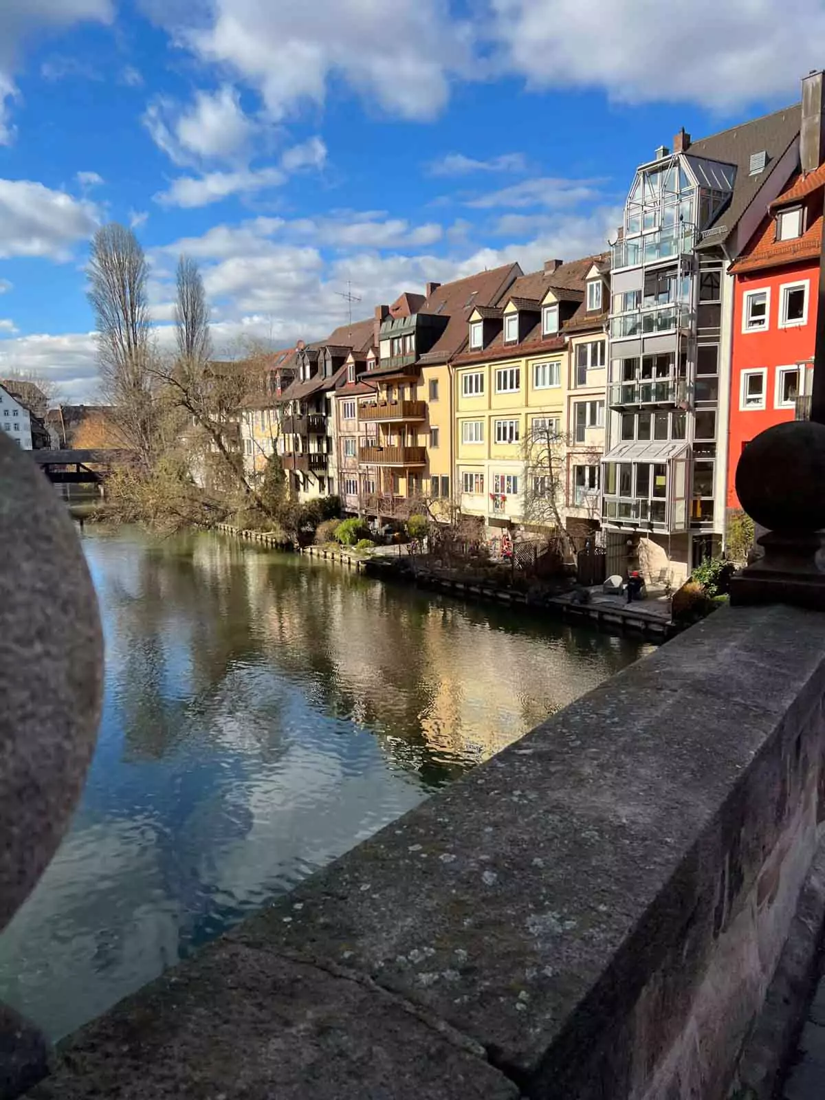 View of the Pegnitz River in Nuremberg, Germany, lined with charming yellow, orange, and red historic buildings reflected in the calm water, capturing the city’s picturesque Old Town atmosphere.