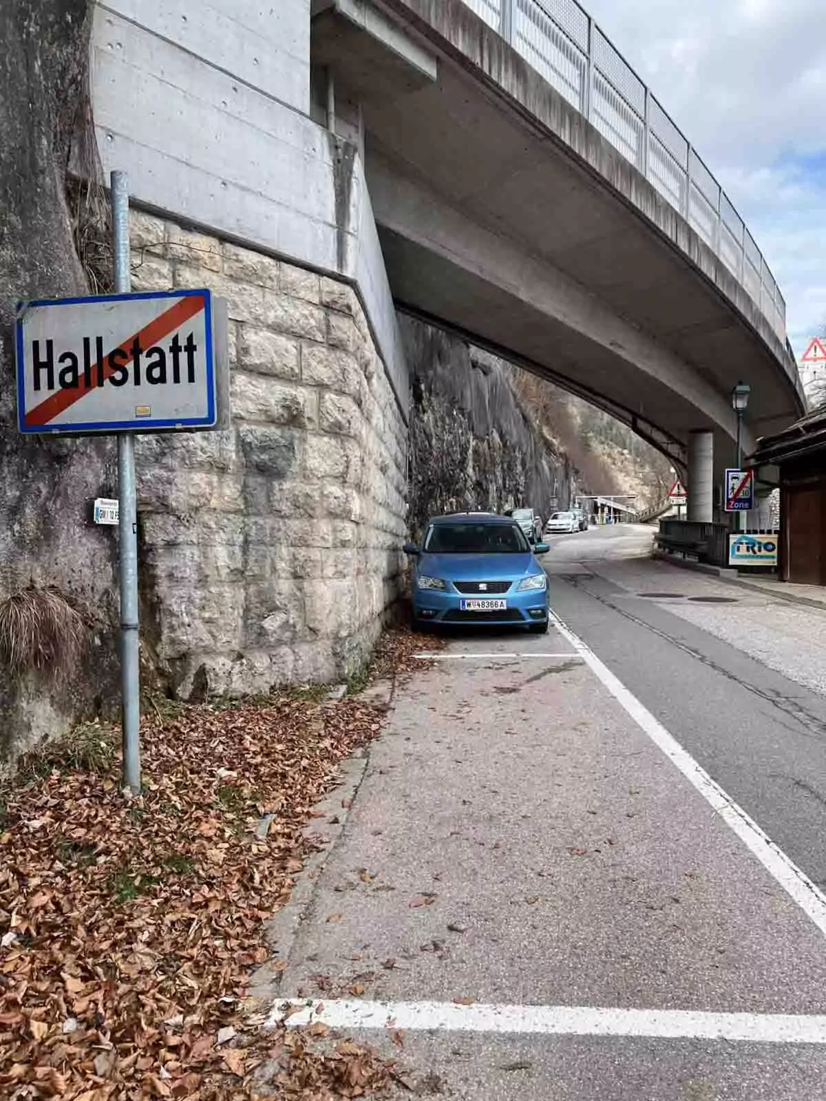 Road sign marking the exit from Hallstatt, Austria, with the village name crossed out, set along a scenic route surrounded by alpine mountains.