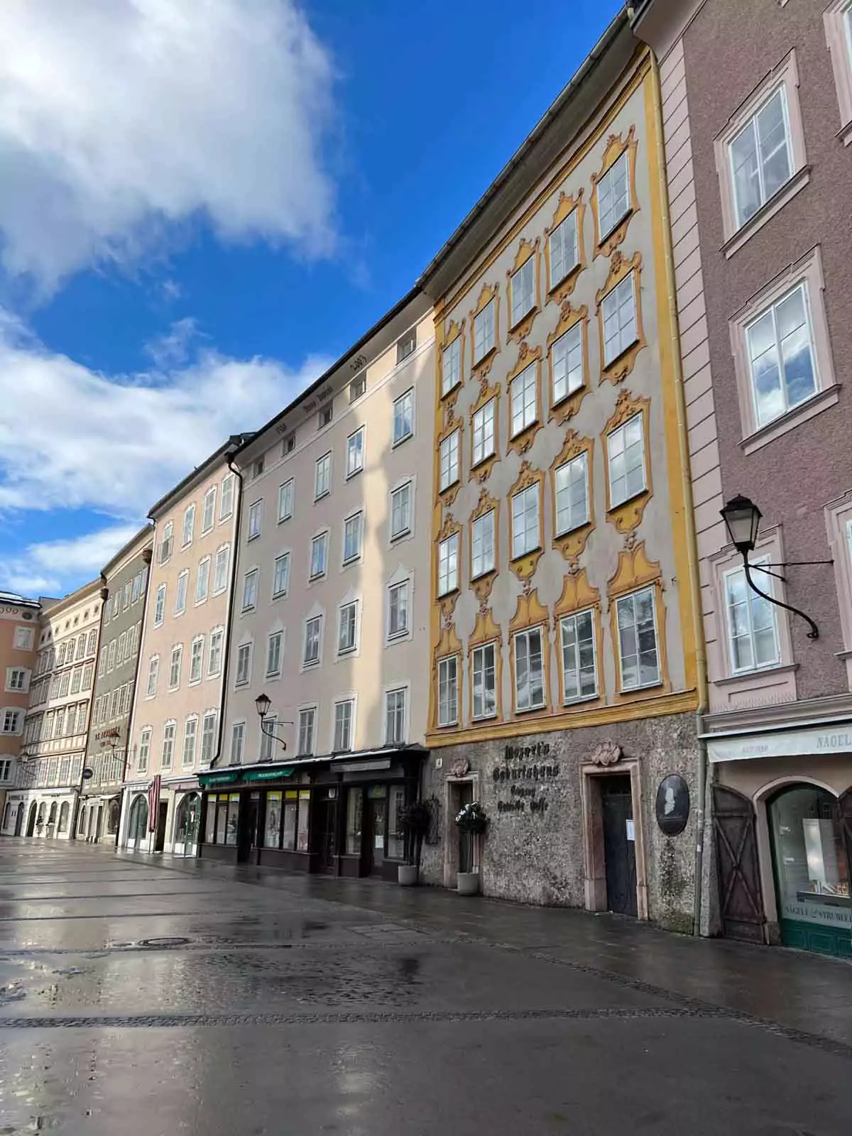 Row of pastel-colored buildings in Salzburg’s University Square (Universitätsplatz), Austria, featuring Baroque facades, decorative windows, and ground-floor shops in a lively pedestrian area.