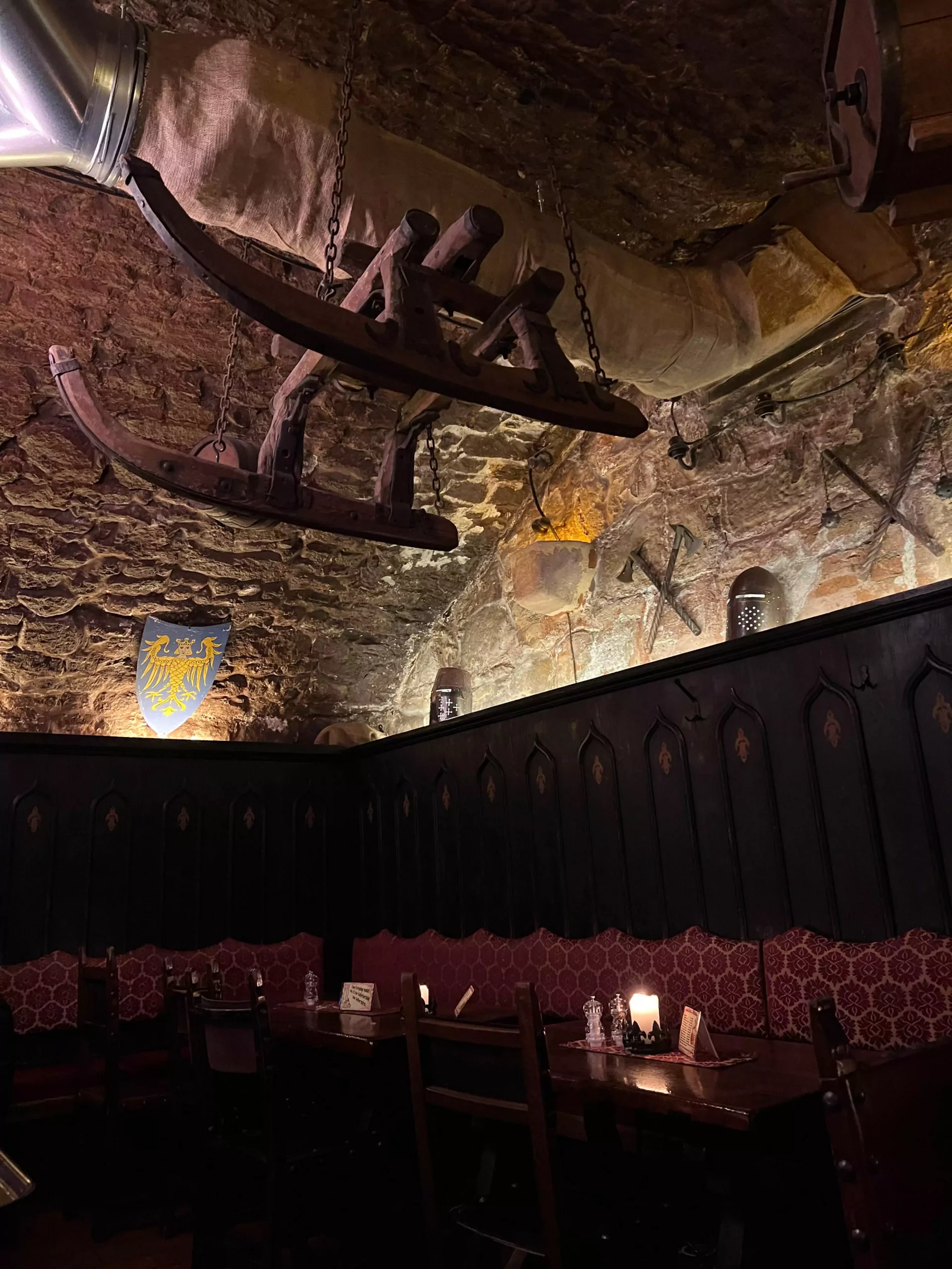 Rustic interior of Im Keller in Nuremberg, Germany, with warm wooden furnishings, exposed brick, and a whimsical wooden shed structure hanging from the ceiling, creating a cozy and unique dining atmosphere.