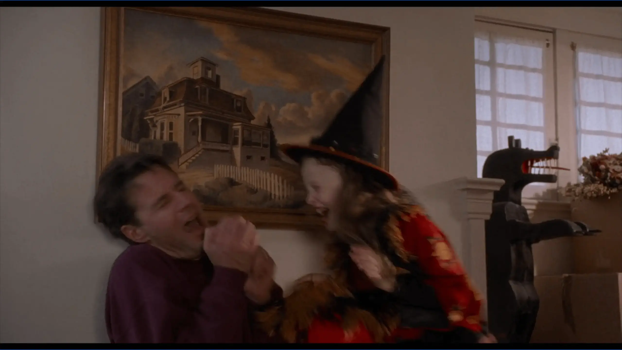 A framed photo on a wall inside Hocus Pocus showing the white colonial-style house at 4 Ocean Avenue, with black shutters and a centered front door. The image captures the iconic setting of Max and Dani’s home in the film.