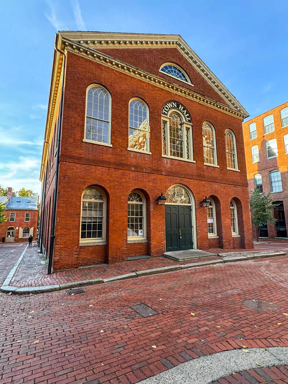Historic red-brick Salem Old Town Hall with symmetrical Federal-style architecture, tall arched windows, and a central white cupola. Built in 1816, it stands as a prominent civic landmark framed by brick-paved walkways.