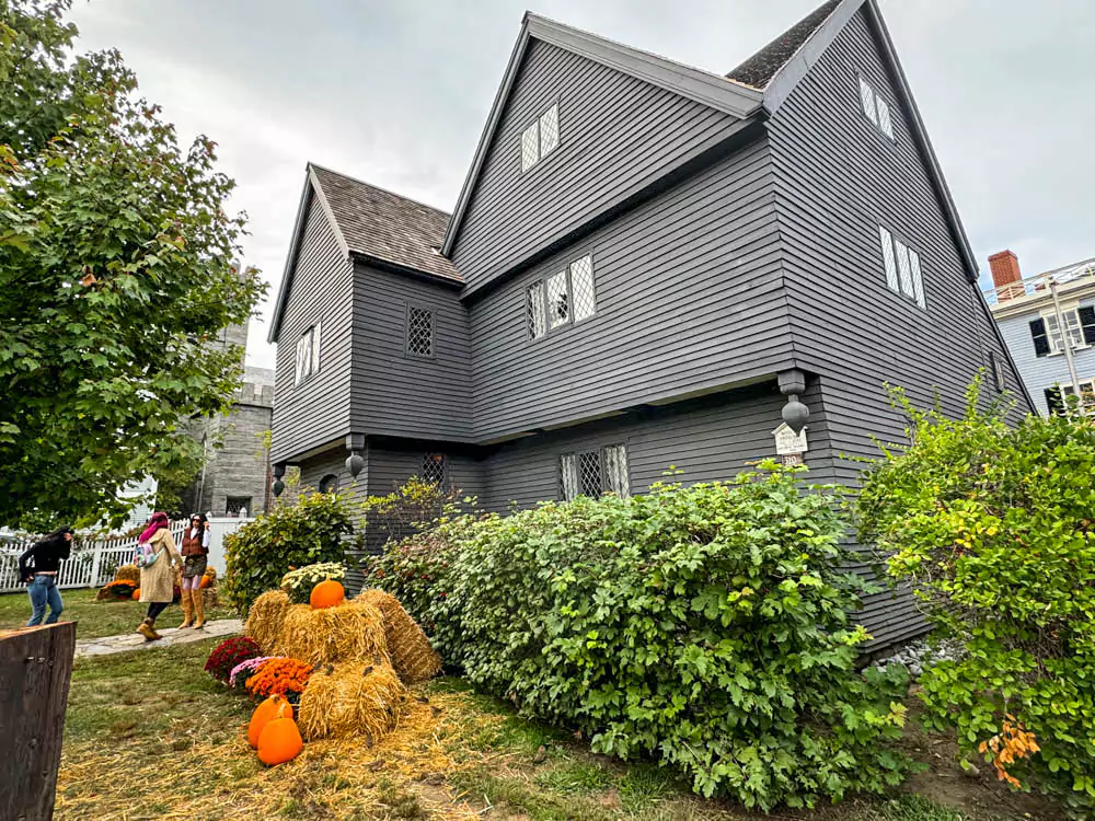 The Witch House in Salem, Massachusetts, during October, featuring its dark timber frame, steep gables, and seasonal decorations like pumpkins and autumn leaves. The historic home of Judge Jonathan Corwin reflects colonial architecture and eerie charm.