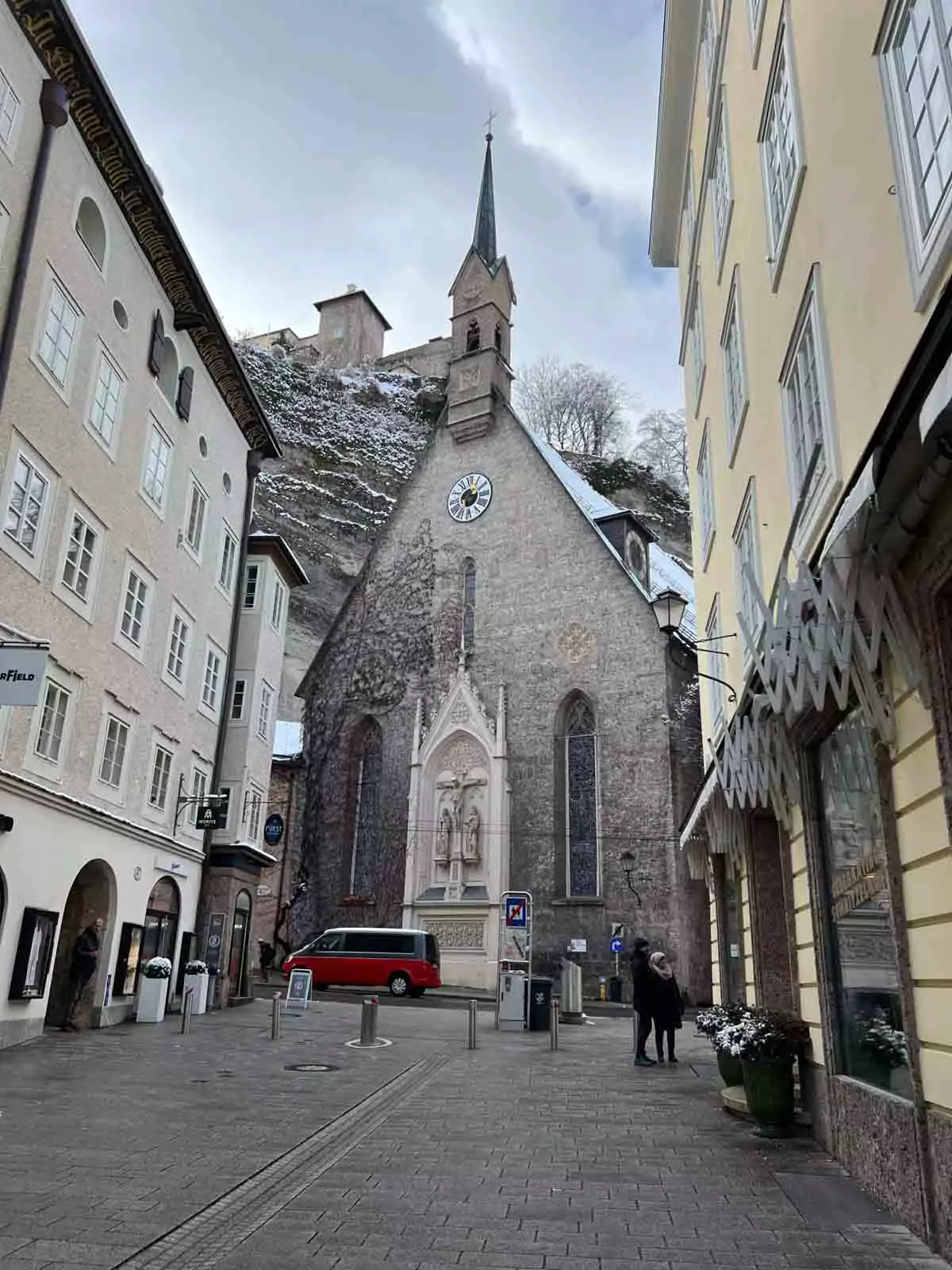 St. Blasius Church in Salzburg’s Old Town, Austria, featuring a Gothic facade with arched windows and a pointed steeple, nestled along narrow historic streets beneath overcast skies.