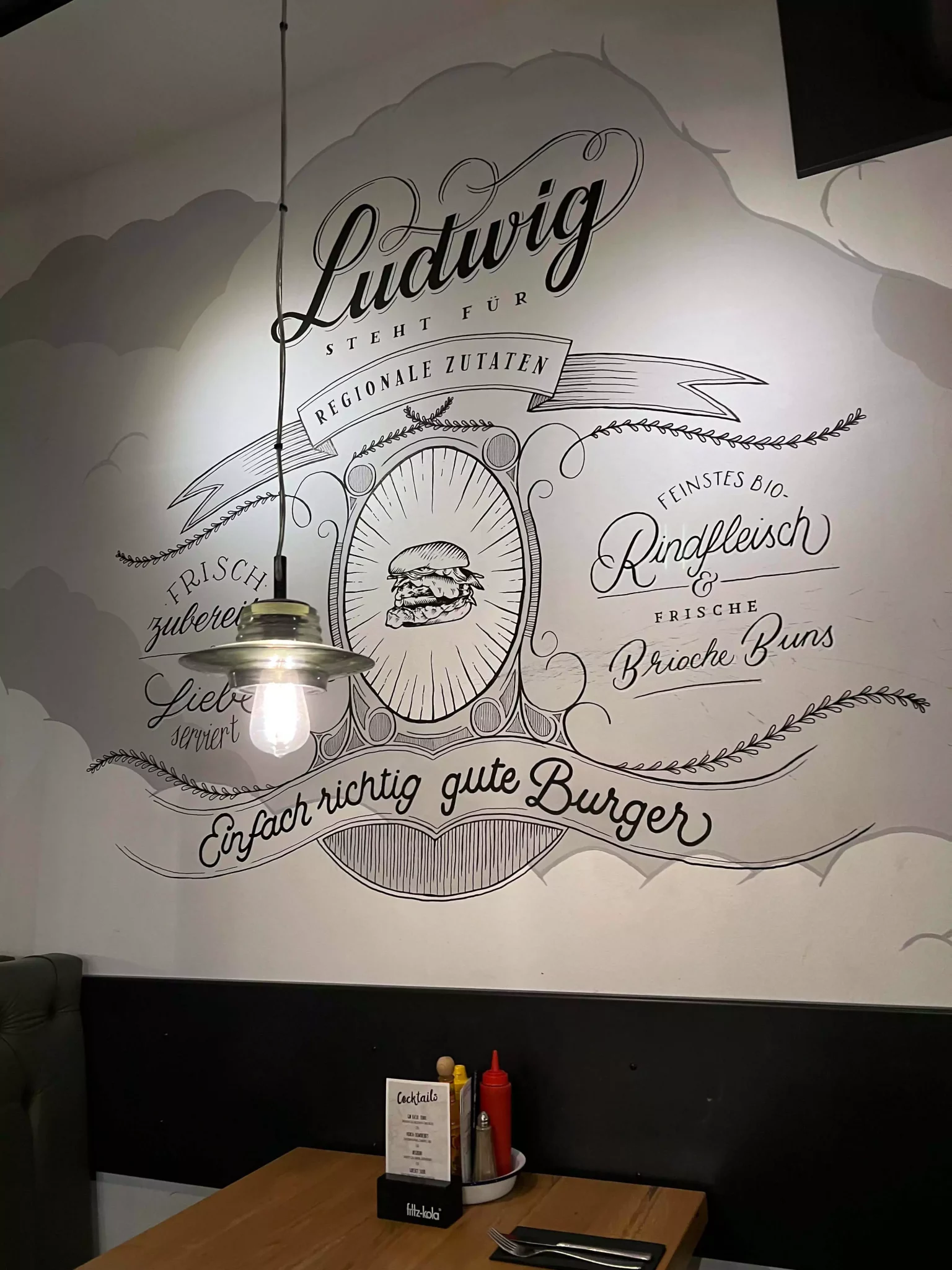 A stylish wall design at Ludwig in Salzburg, Austria, featuring bold typography and modern graphics that reflect the restaurant’s trendy, urban vibe. The artwork adds a playful and creative flair to the casual dining atmosphere.