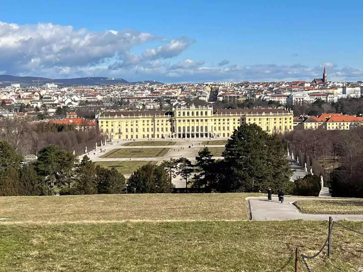 Panoramic view of Schönbrunn Palace from the top of the Gloriette in Vienna, Austria, with the symmetrical Baroque palace gardens in the foreground and the city of Vienna stretching into the distance.