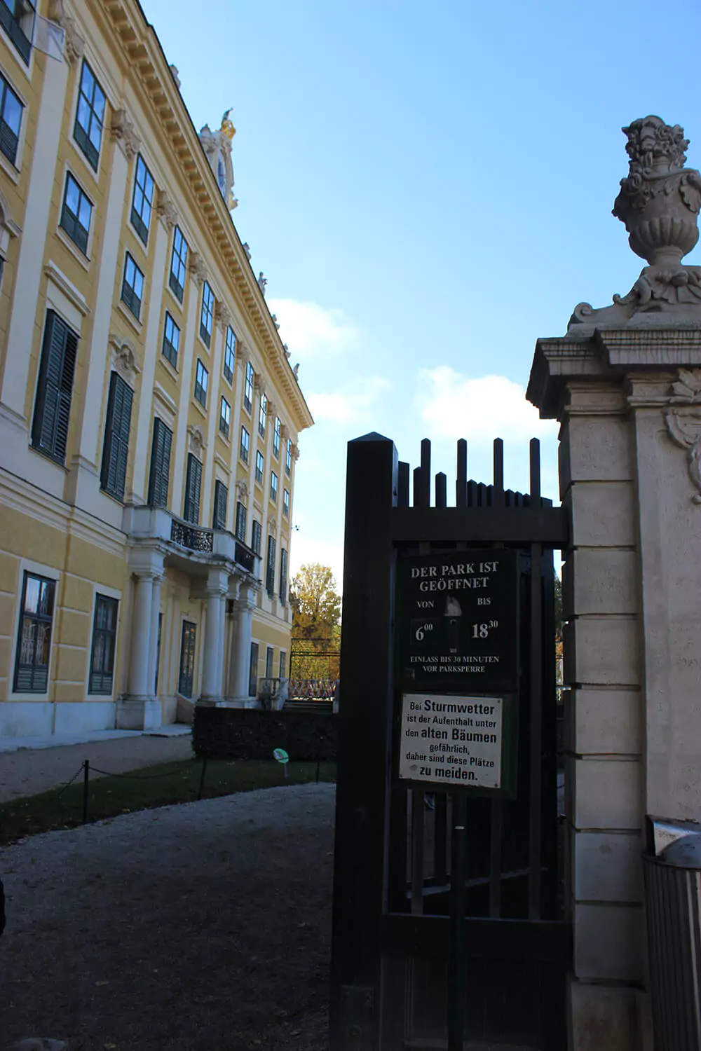 A decorative side gate opens into the gardens at Schönbrunn Palace in Vienna, Austria. The wrought iron gate, framed by manicured hedges and classical stonework, offers a charming, tucked-away entrance to the palace grounds.