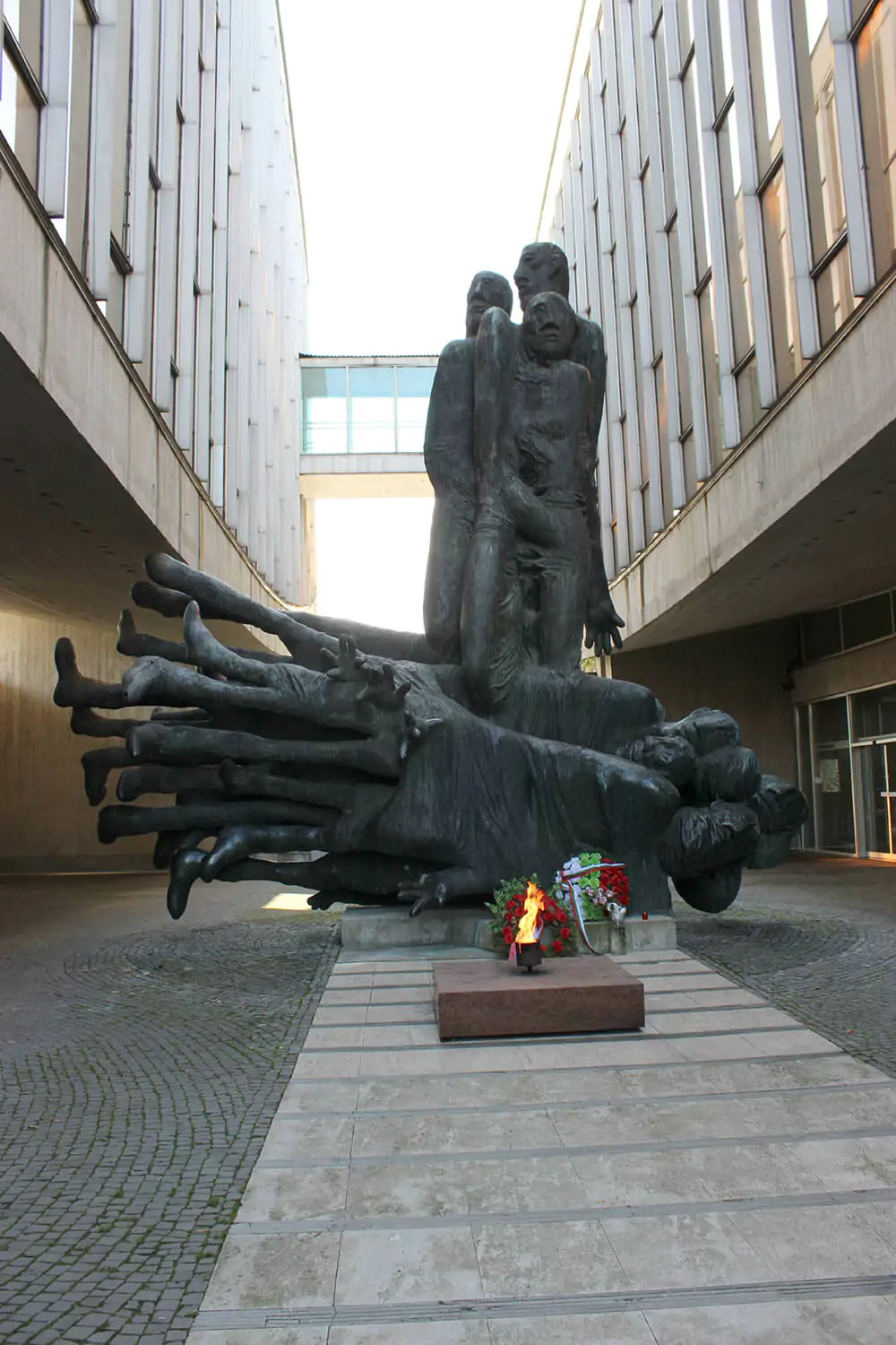 The National Uprising Memorial statue in Banská Bystrica, Slovakia, depicting bold, angular bronze figures symbolizing resistance and courage, set against the dramatic backdrop of the museum’s split concrete architecture
