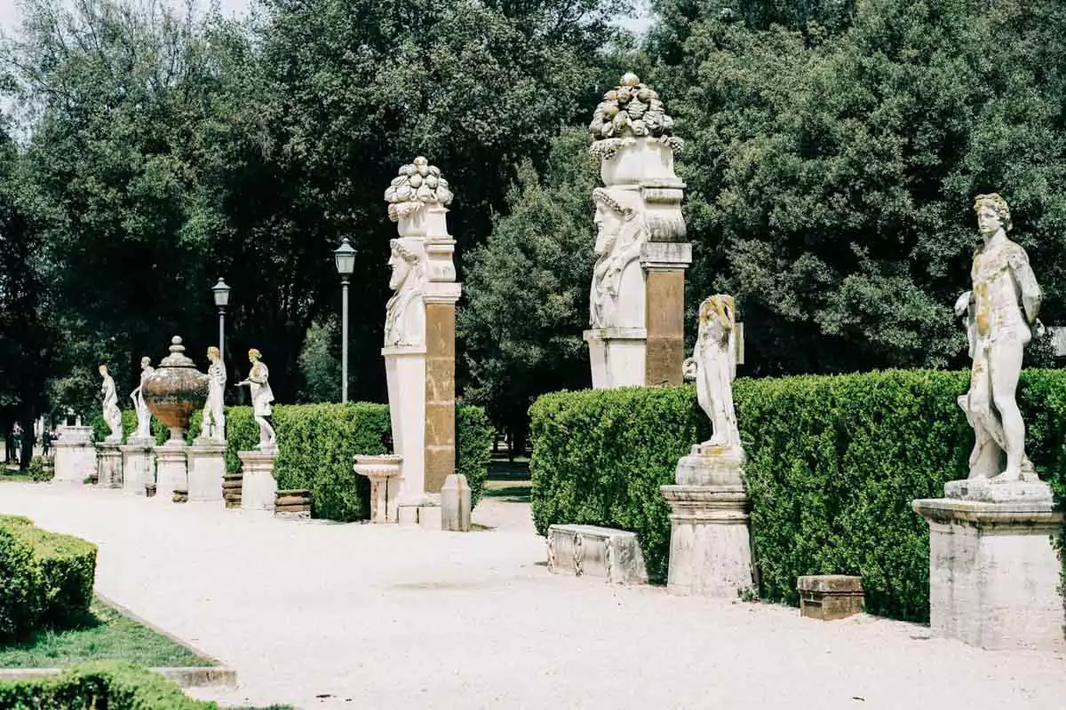 Classical statues in the Borghese Gardens in Rome, Italy, surrounded by manicured greenery and gravel paths, adding an artistic and historic touch to the peaceful park setting.