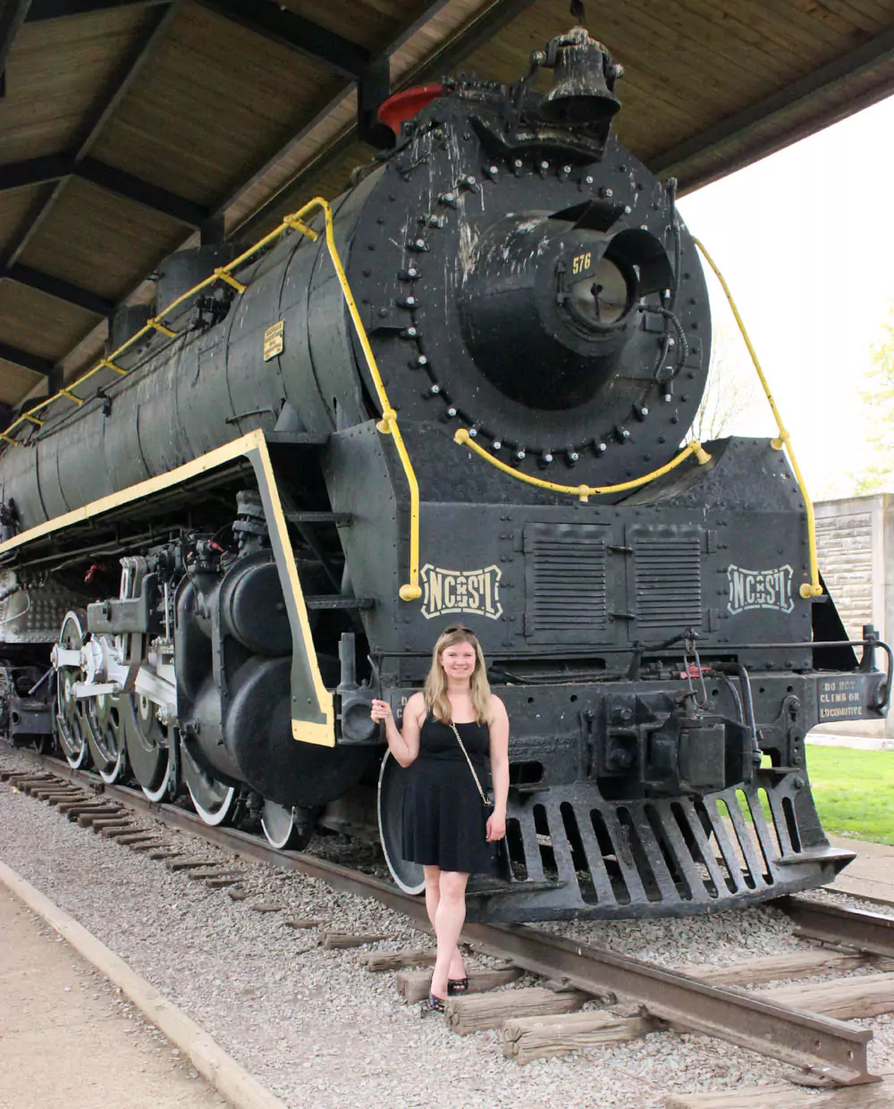 Katie stands beside the historic Chattanooga and St. Louis 576 train displayed in Centennial Park, Nashville, Tennessee. The vintage locomotive is set outdoors with park greenery and clear skies in the background.