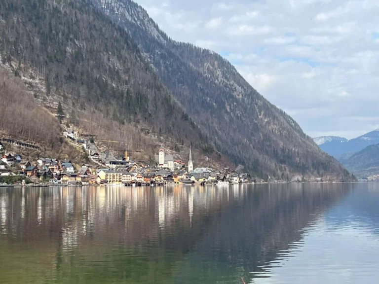 The charming village of Hallstatt, Austria, nestles between steep mountains and the edge of a serene lake. Its pastel-colored houses and pointed church spire reflect in the still water, creating a fairy-tale-like scene straight out of the Alps.