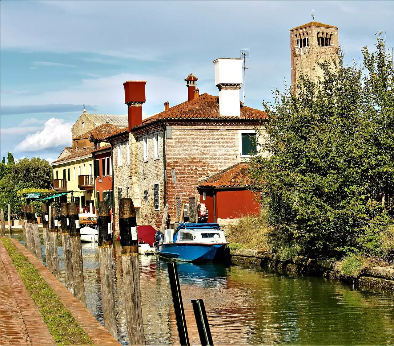 Boats floating in a quiet canal on Torcello Island, Venice, Italy, with ancient brick buildings and Romanesque architecture lining the banks, reflecting the island’s tranquil charm and historic roots.