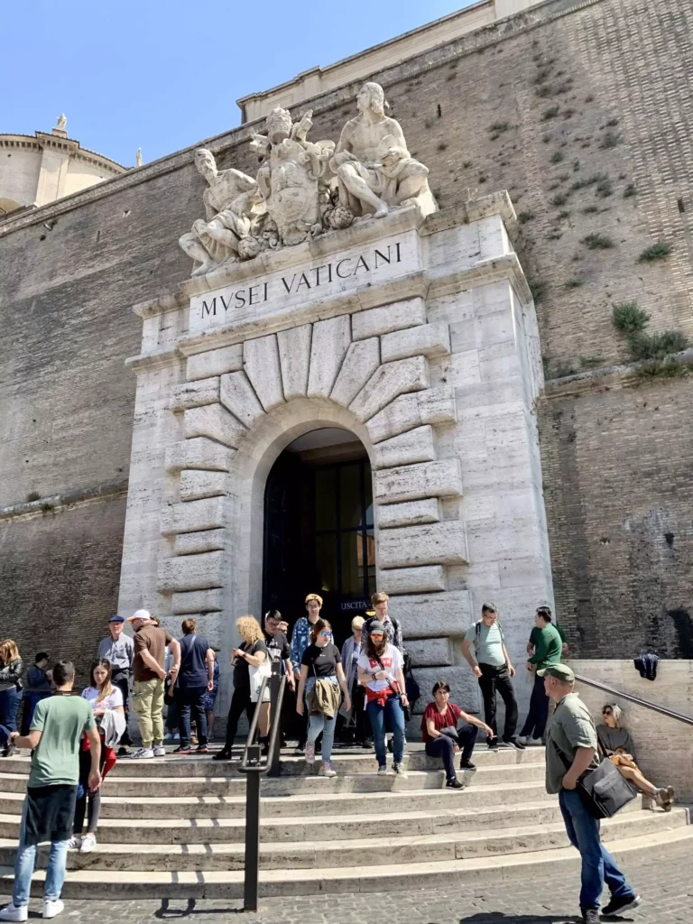 Large stone walls at the entrance to Vatican City, showcasing towering, weathered masonry and a grand arched gateway leading into the historic sovereign city-state.