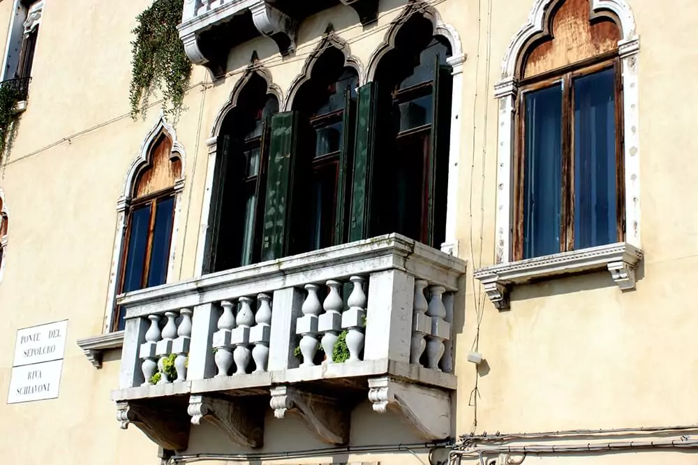 Ornate balcony with arched windows on a historic building near Ponte del Sepolcro in Venice, Italy, featuring detailed stonework and classic Venetian architecture overlooking a quiet canal.