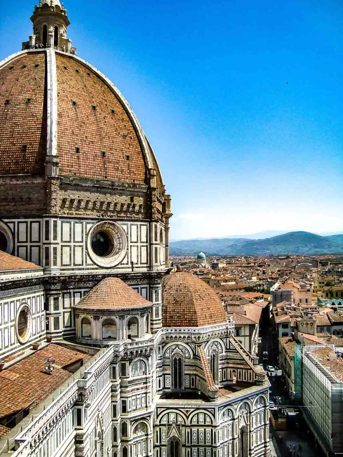 Panoramic view of Florence, Italy, showcasing a sea of terracotta rooftops, historic Renaissance buildings, and iconic landmarks like the Duomo under a Tuscan sky.