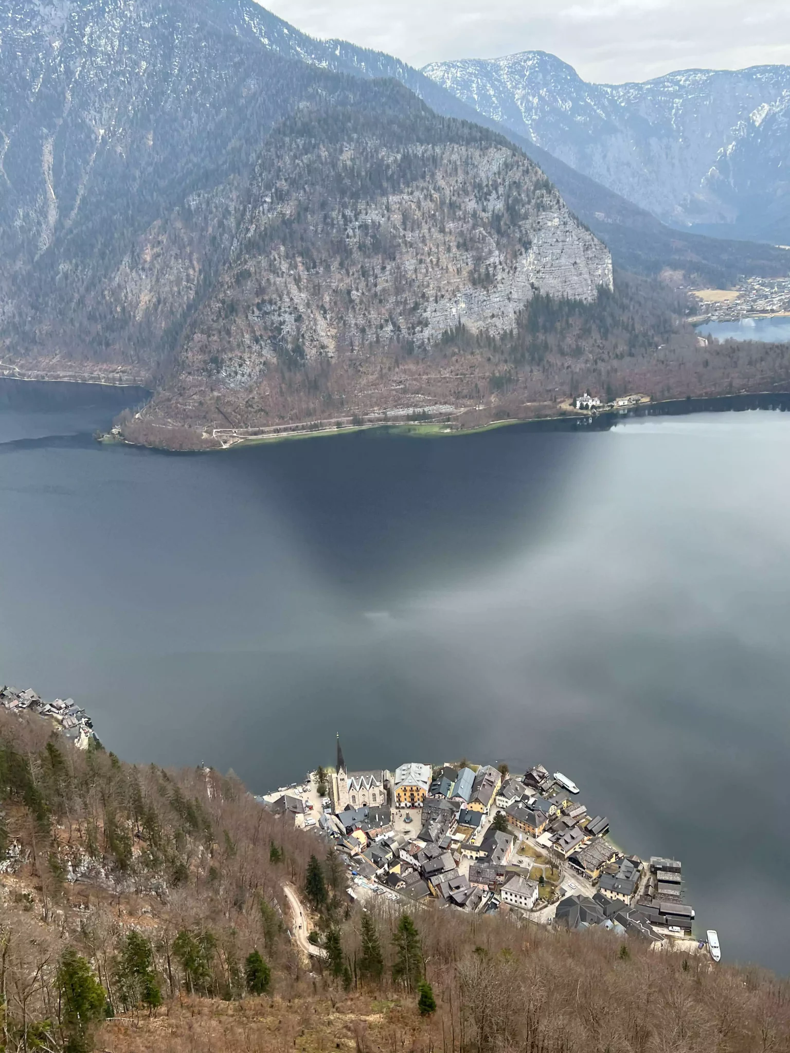 A panoramic view of Hallstatt and its lake from the top of Salzwelten shows the picturesque village nestled between alpine mountains and the shimmering water below. The elevated vantage point offers a stunning, postcard-worthy scene of Austria’s natural and historic beauty.