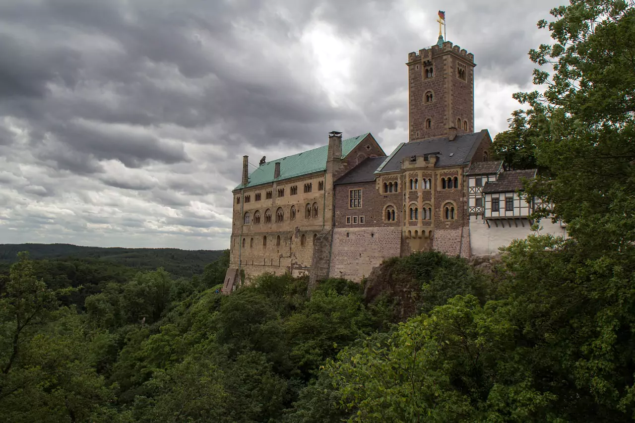 Wartburg Castle in Germany, perched on a forested hilltop with its stone towers and timber-framed sections overlooking the Thuringian countryside