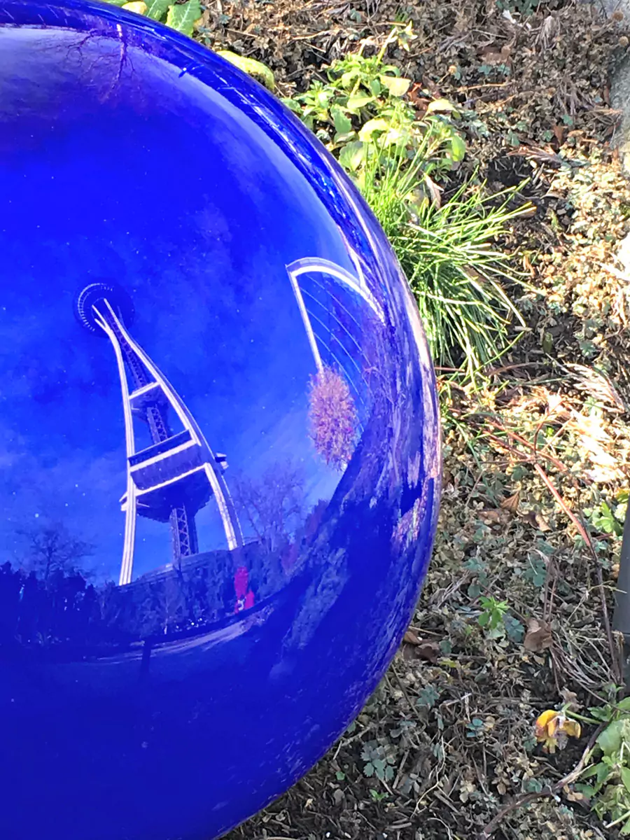 The Space Needle reflected in a shiny Chihuly glass sculpture at the Chihuly Garden and Glass Museum in Seattle. The curved, colorful glass creates a distorted yet artistic mirror image of the iconic tower, blending art with skyline.