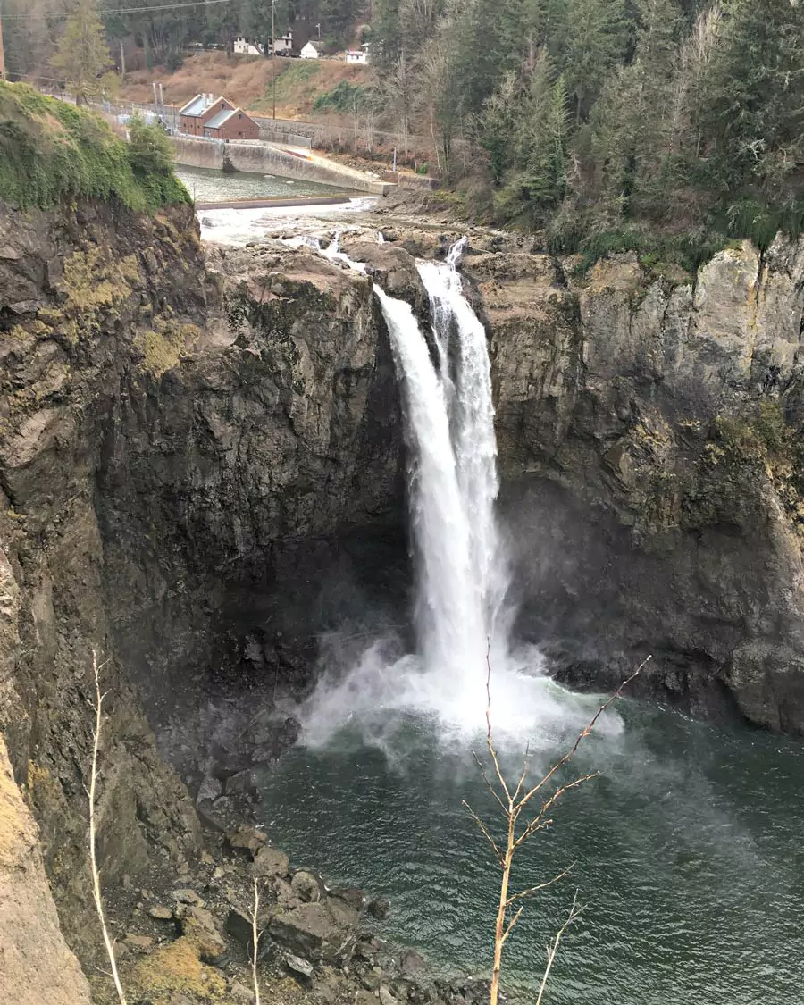Snoqualmie Falls near Seattle, Washington, cascading powerfully over a rocky cliff surrounded by lush green forest. Mist rises from the base of the waterfall, creating a dramatic and scenic Pacific Northwest landscape.