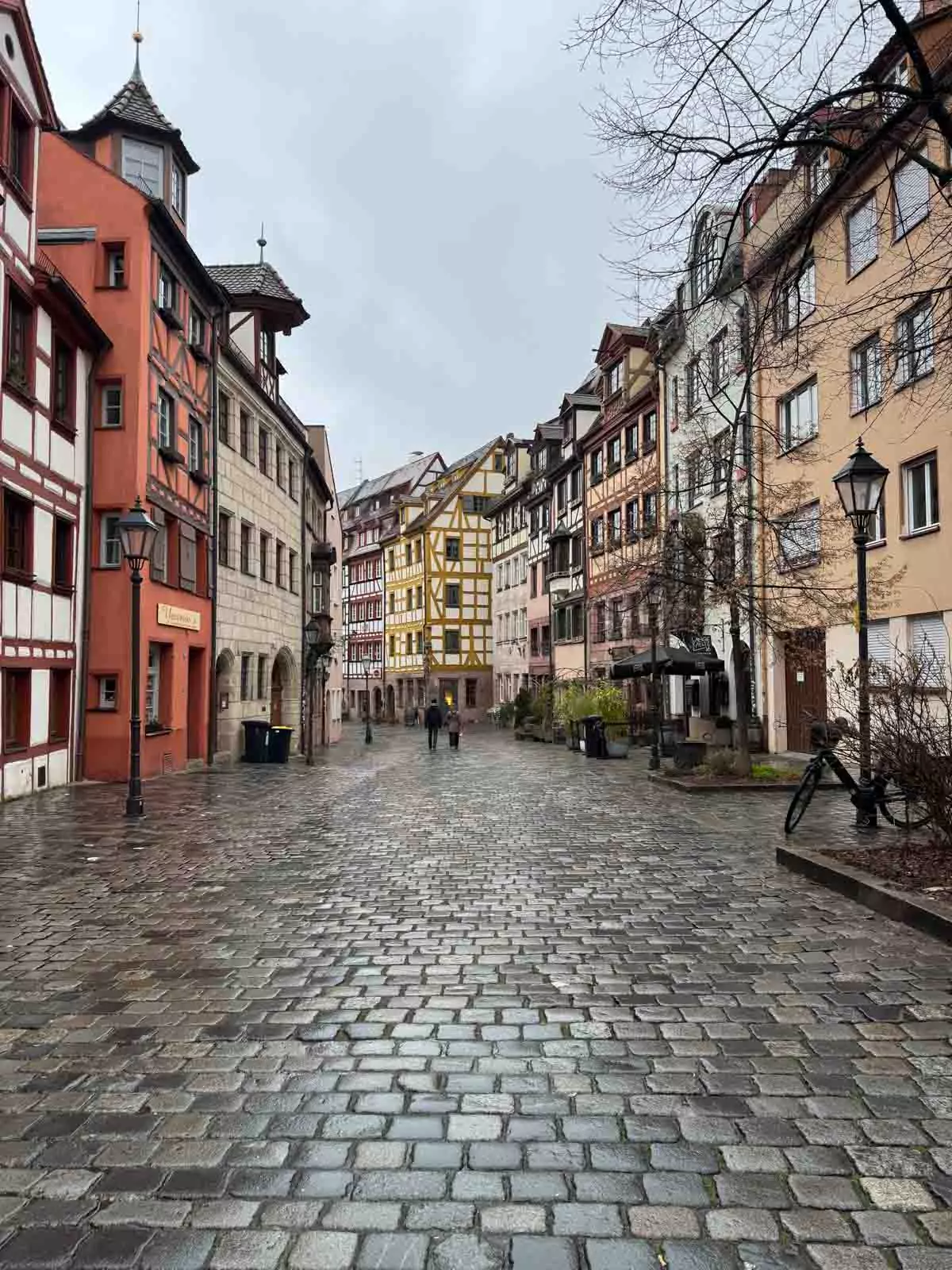 Charming Weißgerbergasse street in Nuremberg, Germany, glistening with rain as colorful half-timbered houses reflect on the wet cobblestones under gray skies.