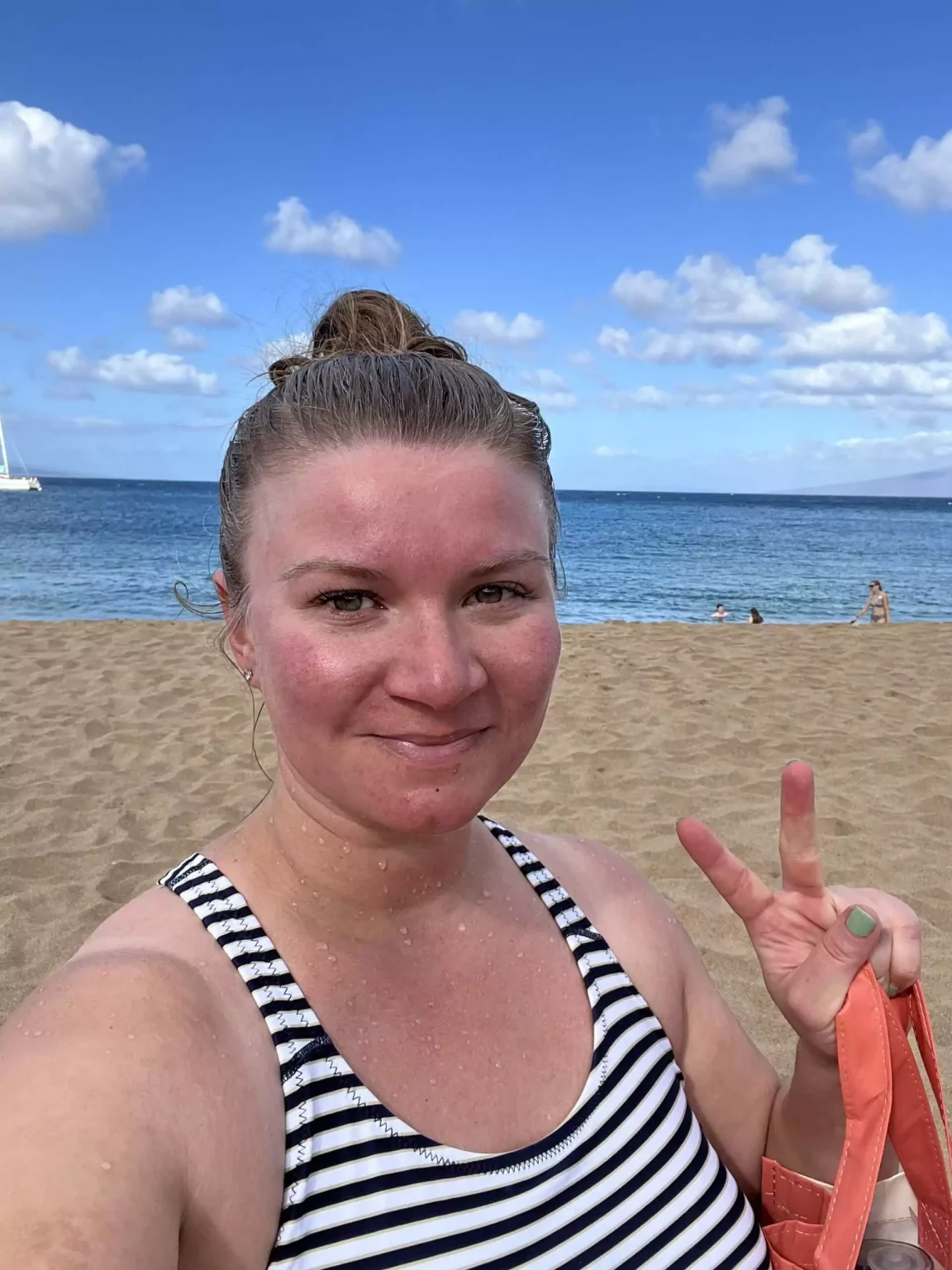 Katie taking a selfie on a Maui beach, wearing a stylish swimsuit with a lightweight cover-up and sunglasses. The ocean waves and palm trees in the background highlight her relaxed, sun-ready look perfect for a day by the water in Hawaii.
