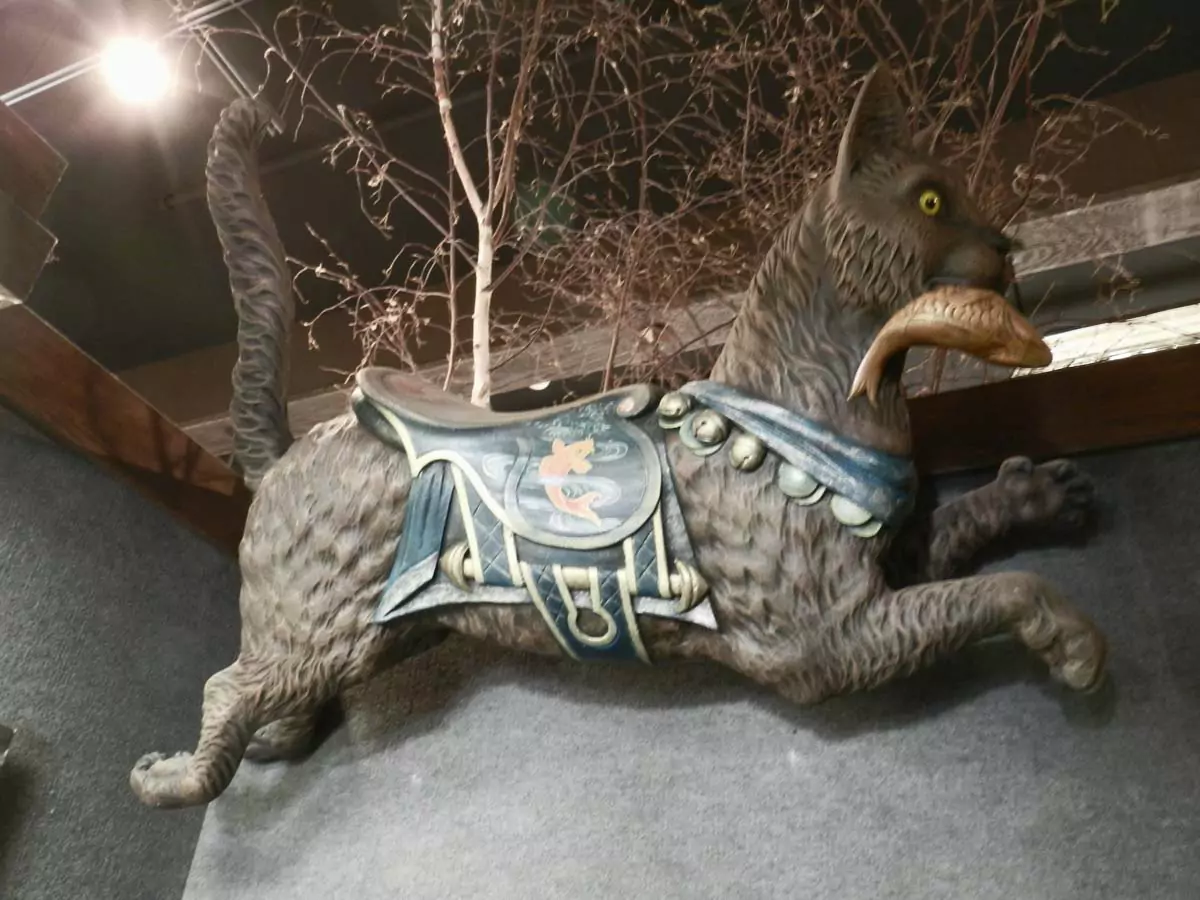 Carved carousel seat shaped like a large cat with detailed fur and expressive face, displayed on a wall at the House on the Rock in Wisconsin, part of its weird Wisconsin roadside attractions collection.